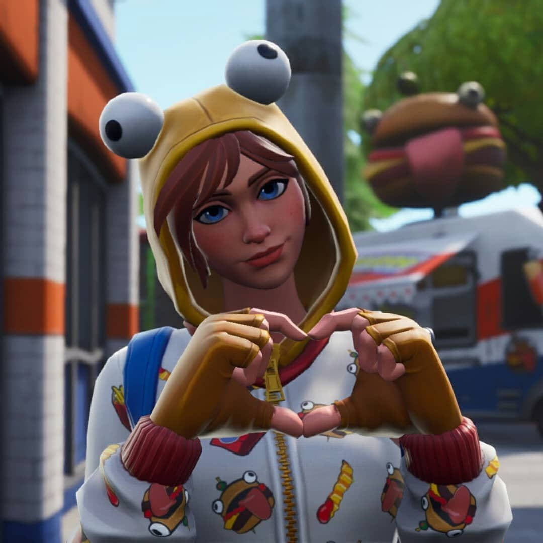 電玩遊戲 桌布 壁紙 — 一個穿著黃色青蛙連帽衫的Fortnite角色在陽光明媚的城市背景下用手比出心形。