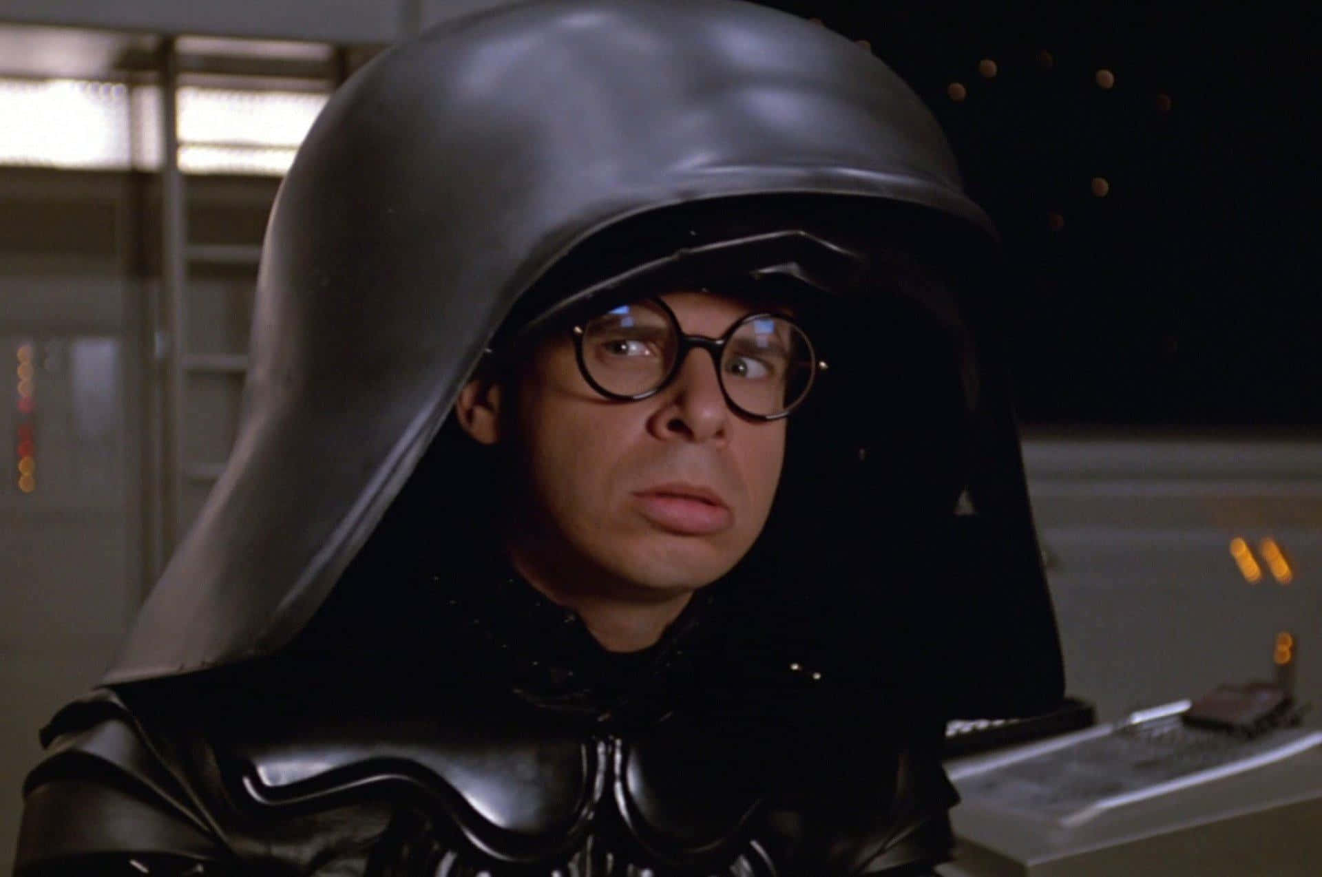 rick moranis 桌布 壁紙 — 一個穿著黑武士服裝、戴著圓框眼鏡的男人在昏暗的科幻場景中向上看。