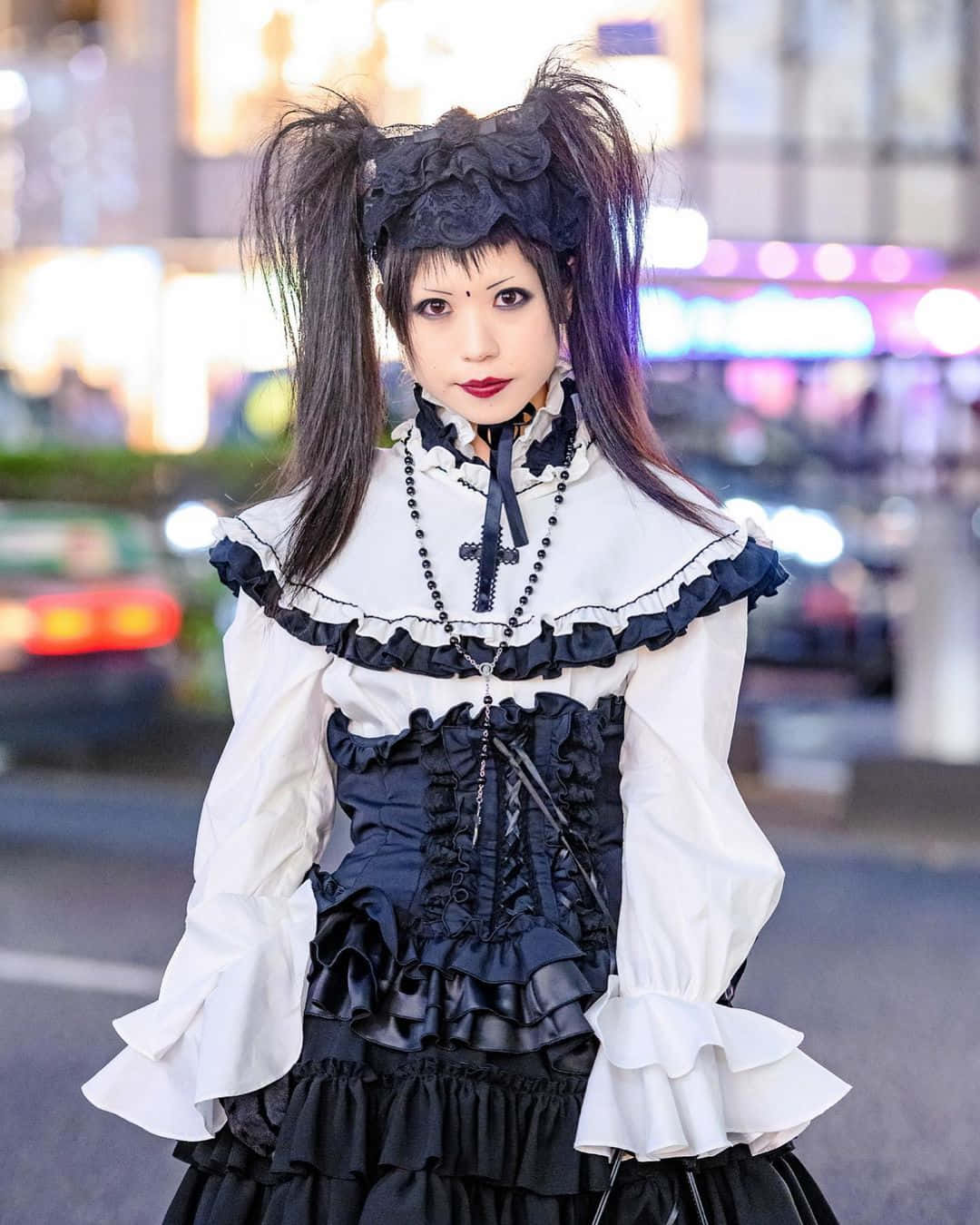 Visual Kei 桌布 壁紙 — 一個穿著黑白哥德蘿莉塔服裝、紮著雙馬尾的人，夜晚站在霓虹燈模糊的城市街道上。