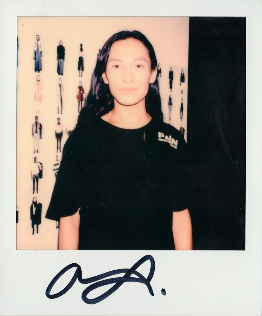 Alexander Wang 桌布 壁紙 — 一個穿著黑色「PAIN」T恤的人站在一面展示垂直排列時尚人體模型的牆前，照片呈拍立得風格。