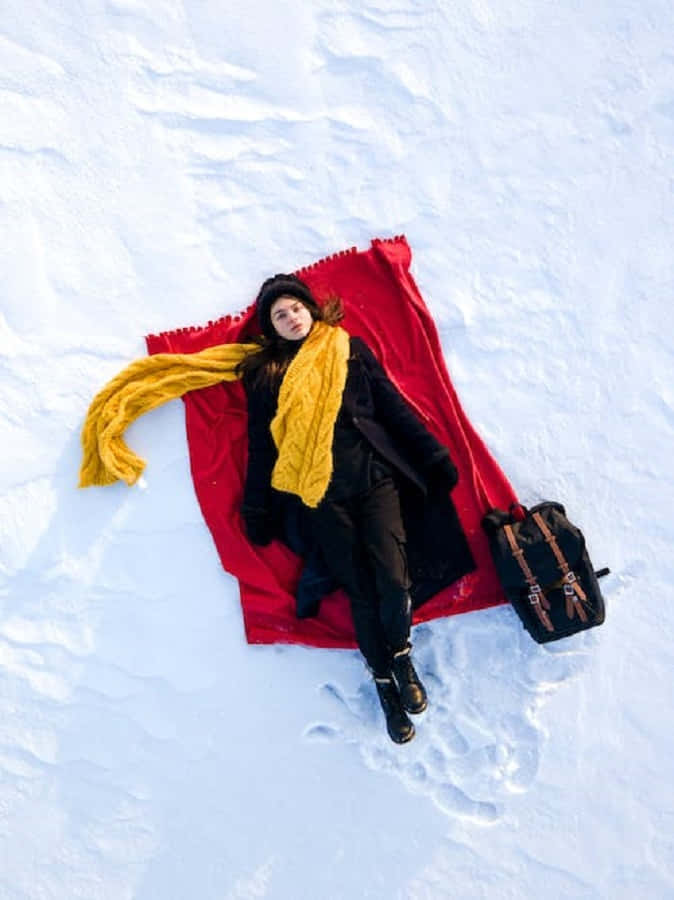 Snowshoes 桌布 壁紙 — 一個穿著黑色冬季裝備和黃色圍巾的人躺在紅色毯子上，身處新雪中，附近有一個背包。
