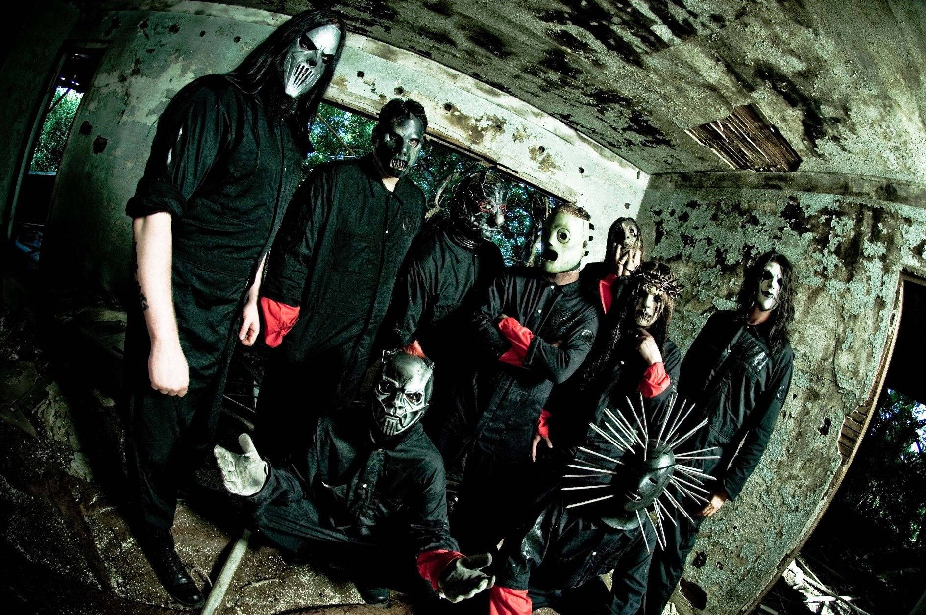 Slipknot 桌布 壁紙 — 一個穿著黑色服裝和怪誕面具的樂隊在腐朽的混凝土結構內擺出威脅性的姿勢。