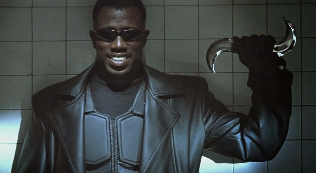 Wesley Snipes 桌布 壁紙 — 一個穿著黑色皮夾克和太陽眼鏡的男人，手持彎曲的銀色刀片對著瓷磚牆。