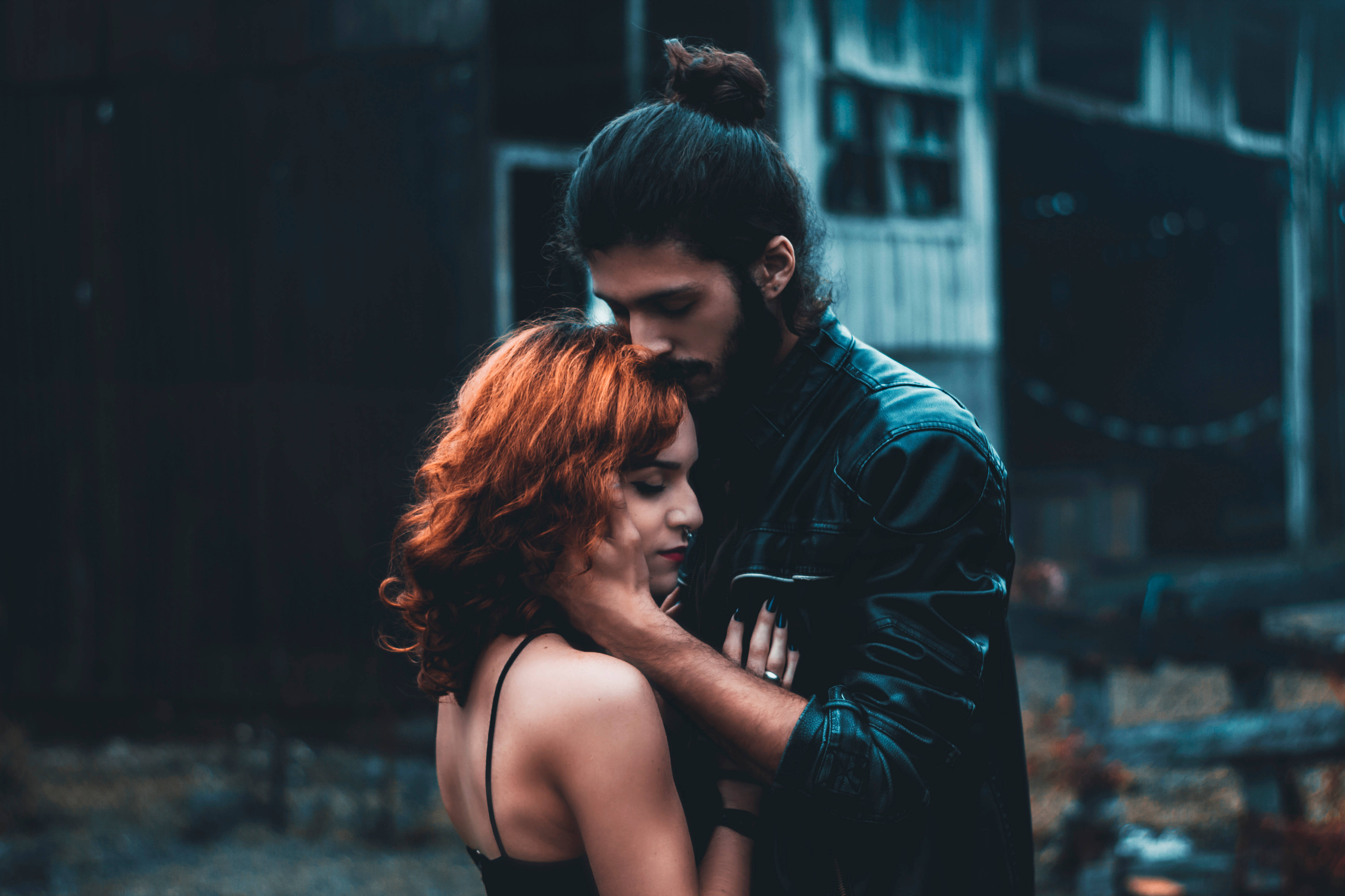 extremely cute 桌布 壁紙 — 一個穿著黑色皮夾克的男人，在昏暗的城市背景下，溫柔地擁抱一個有著火紅頭髮的女人。