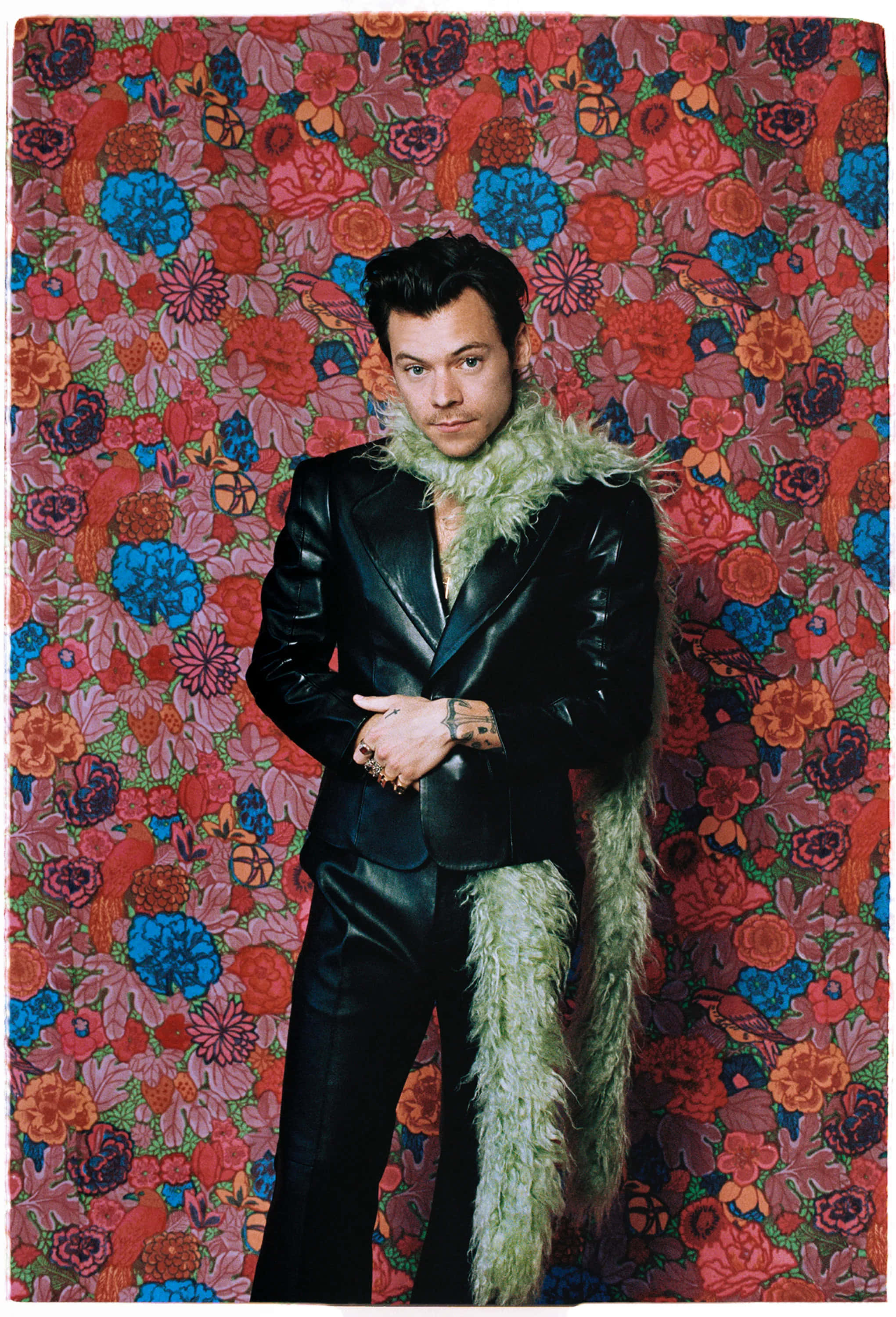 Harry Styles 2021 桌布 壁紙 — 一個穿著黑色皮套裝、綠色毛領的男人，自信地站在鮮豔的花卉壁紙背景前。