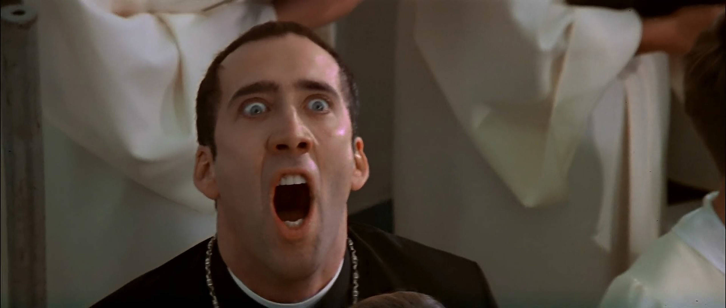 nicolas cage meme 桌布 壁紙 — 一個穿著黑色神職人員領的男人在昏暗的房間裡，身後有白色長袍，睜大眼睛張開嘴巴尖叫。