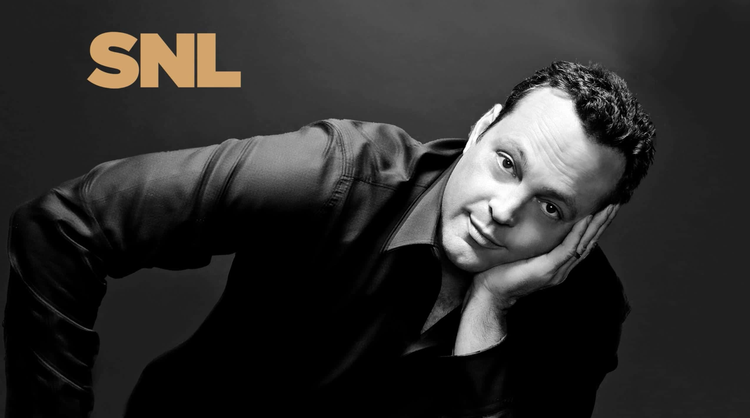 Vince Vaughn 桌布 壁紙 — 一個穿著黑色襯衫的男人，在帶有SNL標誌的暗色工作室背景中，用手托著頭，露出頑皮的假笑。