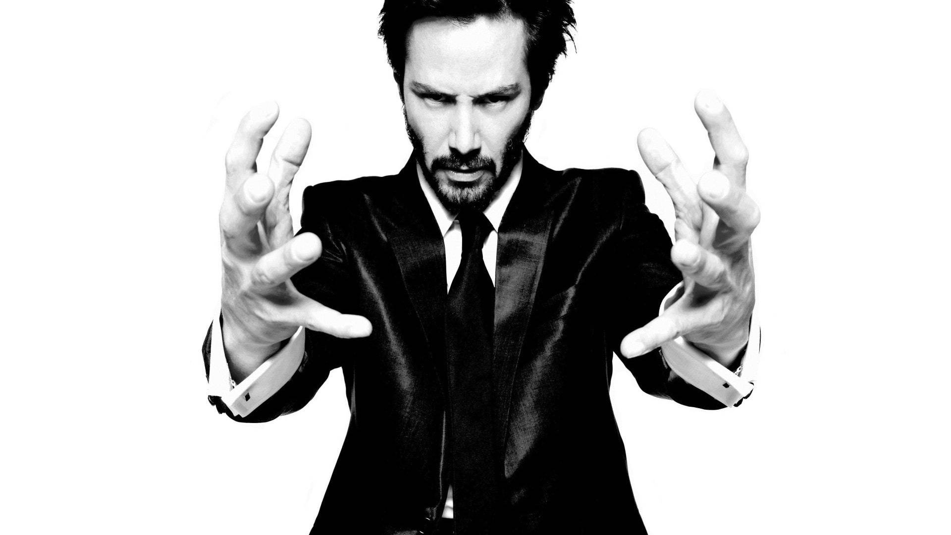John Wick 桌布 壁紙 — 一個穿著黑色西裝、表情強烈、雙手伸出的男人，背景是純白色。