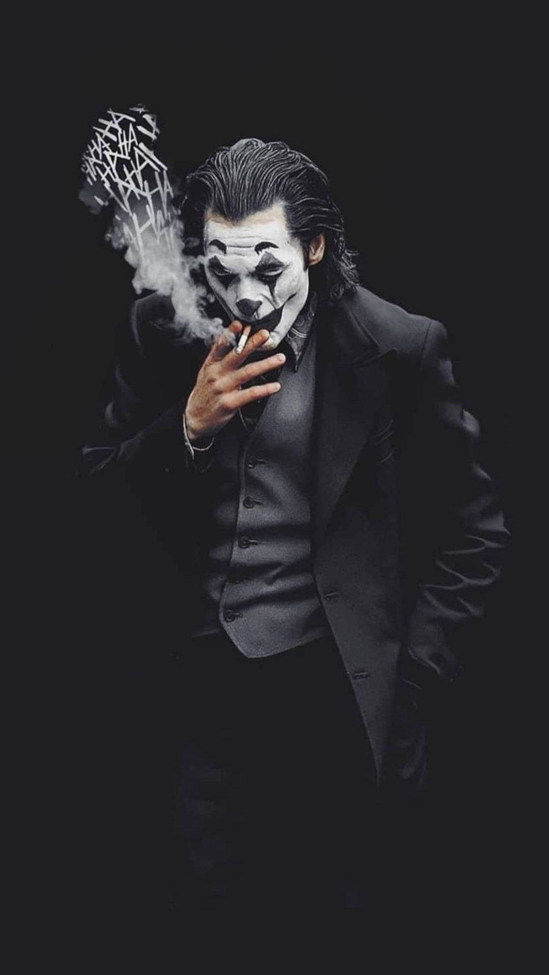 小丑 桌布 壁紙 — 一個穿著黑色西裝的男人抽煙，煙霧在他頭頂形成一個鋸齒狀的面具，背景為深色。