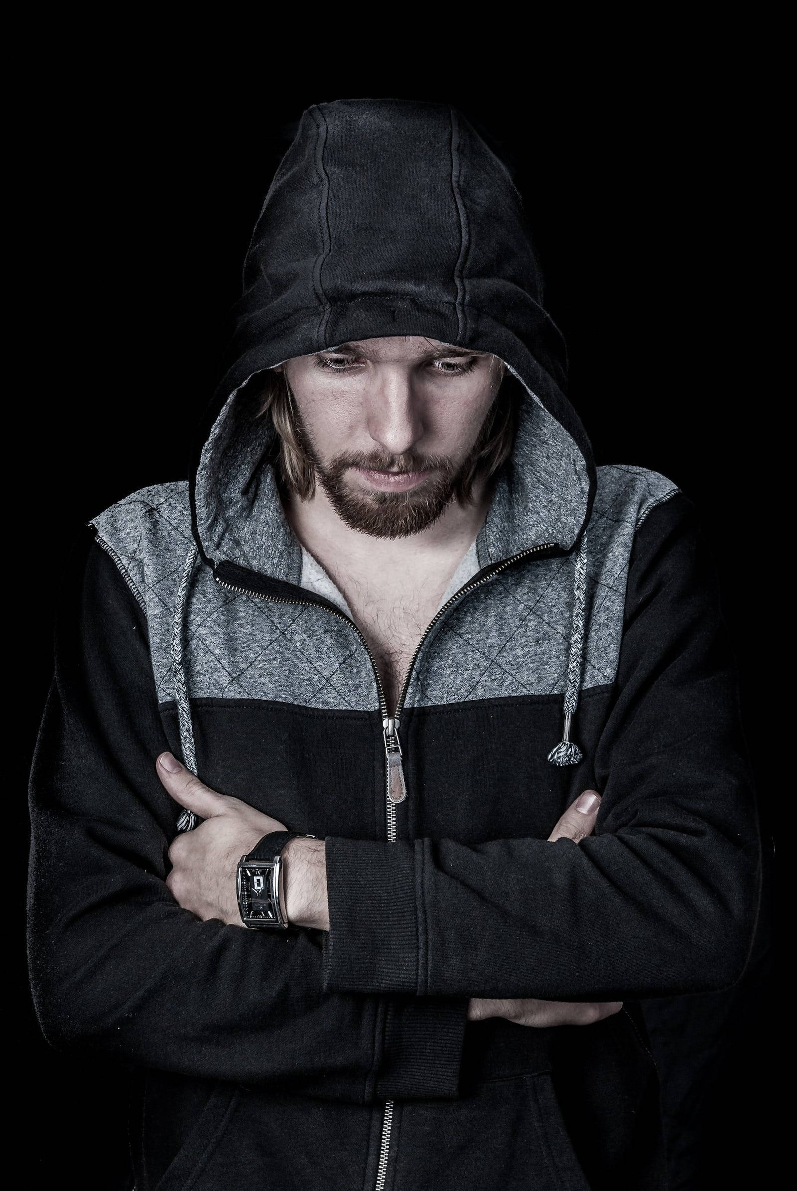Handsome Boy 桌布 壁紙 — 一個穿著黑色連帽外套的男人，雙臂交叉，站在黑暗背景前，低頭表情嚴肅。