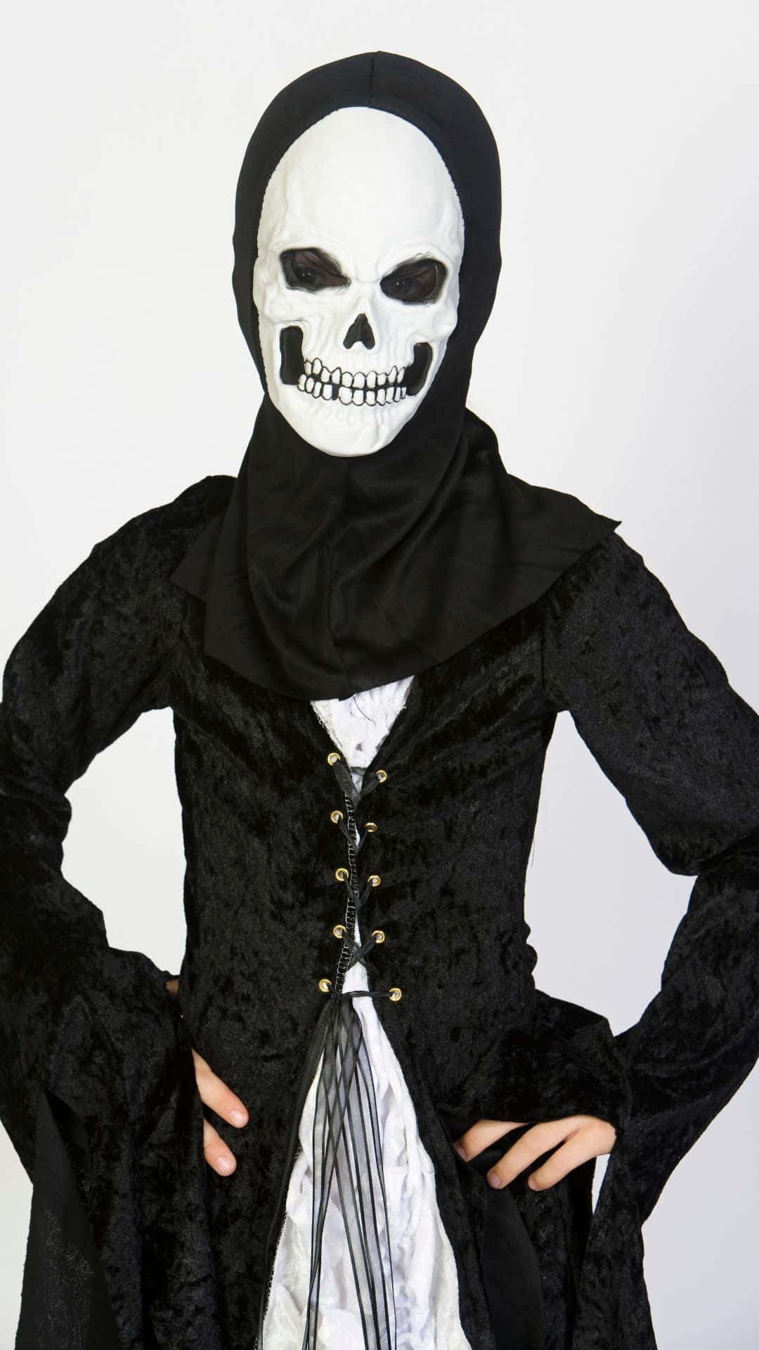 Skeleton Costumes 桌布 壁紙 — 一個穿著黑色連帽服裝的人，戴著白色骷髏面具，面具上有黑色眼窩和牙齒，背景為純白色。