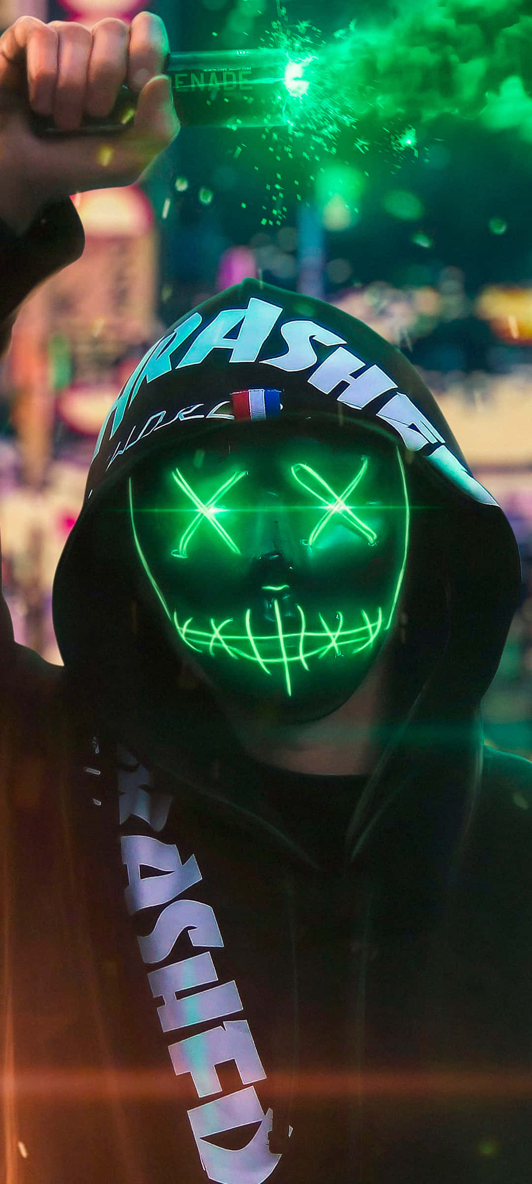 Mask 桌布 壁紙 — 一個穿著黑色連帽衫、戴著發光綠色骷髏面具的人，在充滿活力的音樂會上拿著螢光棒。