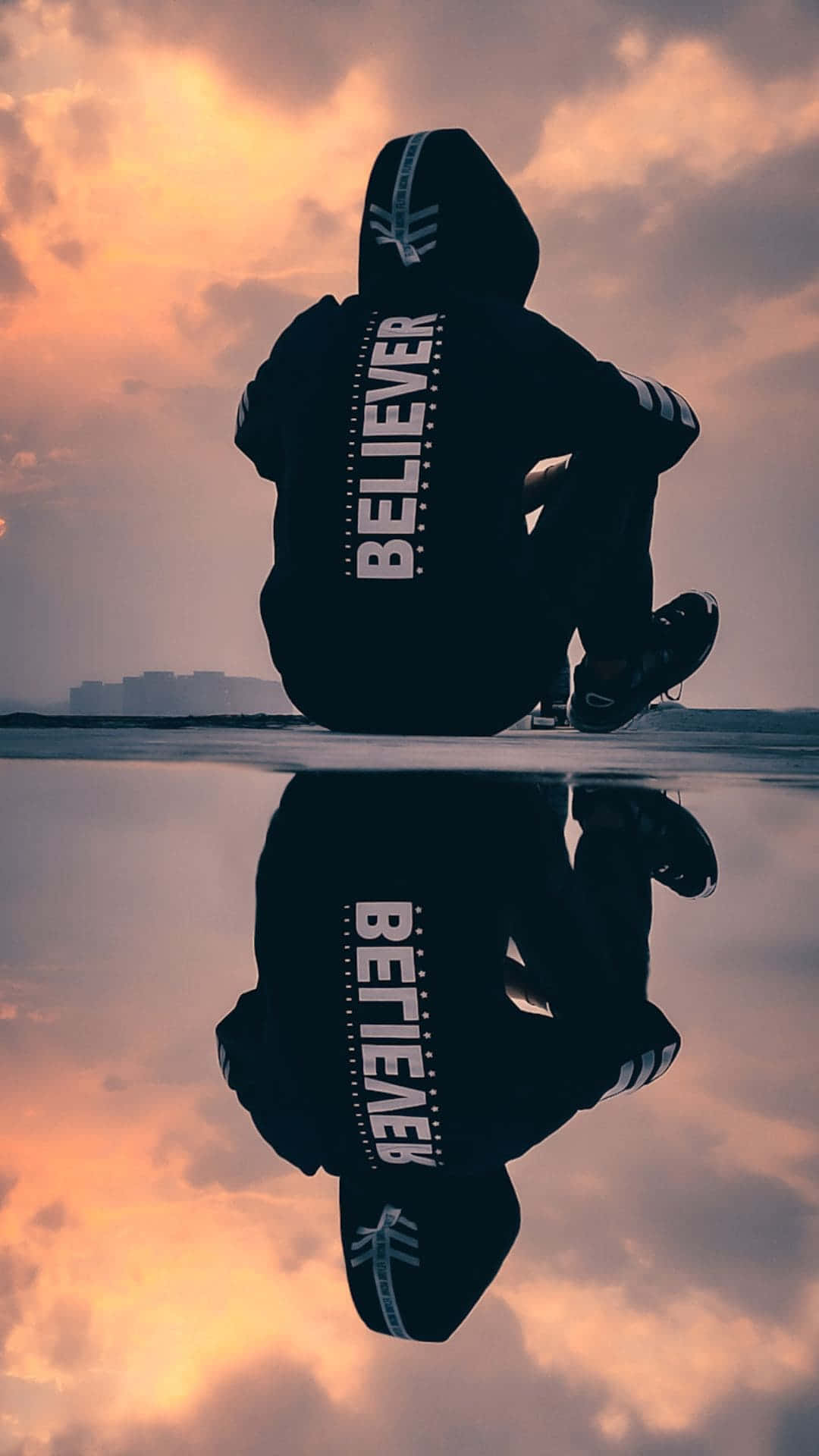 穿著 believer 連帽衫的人坐在水邊，帶有日落倒影的剪影。 — 憂鬱男孩 壁紙