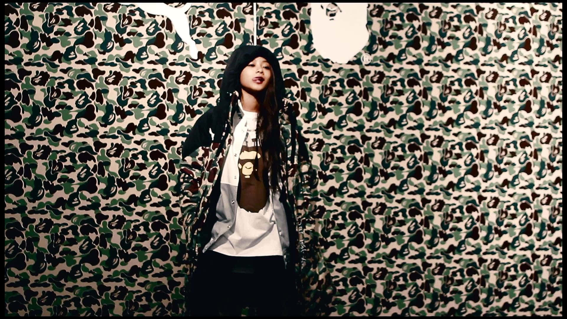 Bape 動態 桌布 壁紙 — 一個穿著黑色連帽衫和分層街頭服飾的人站在一面大膽的迷彩圖案牆前，牆上掛著白色面具。