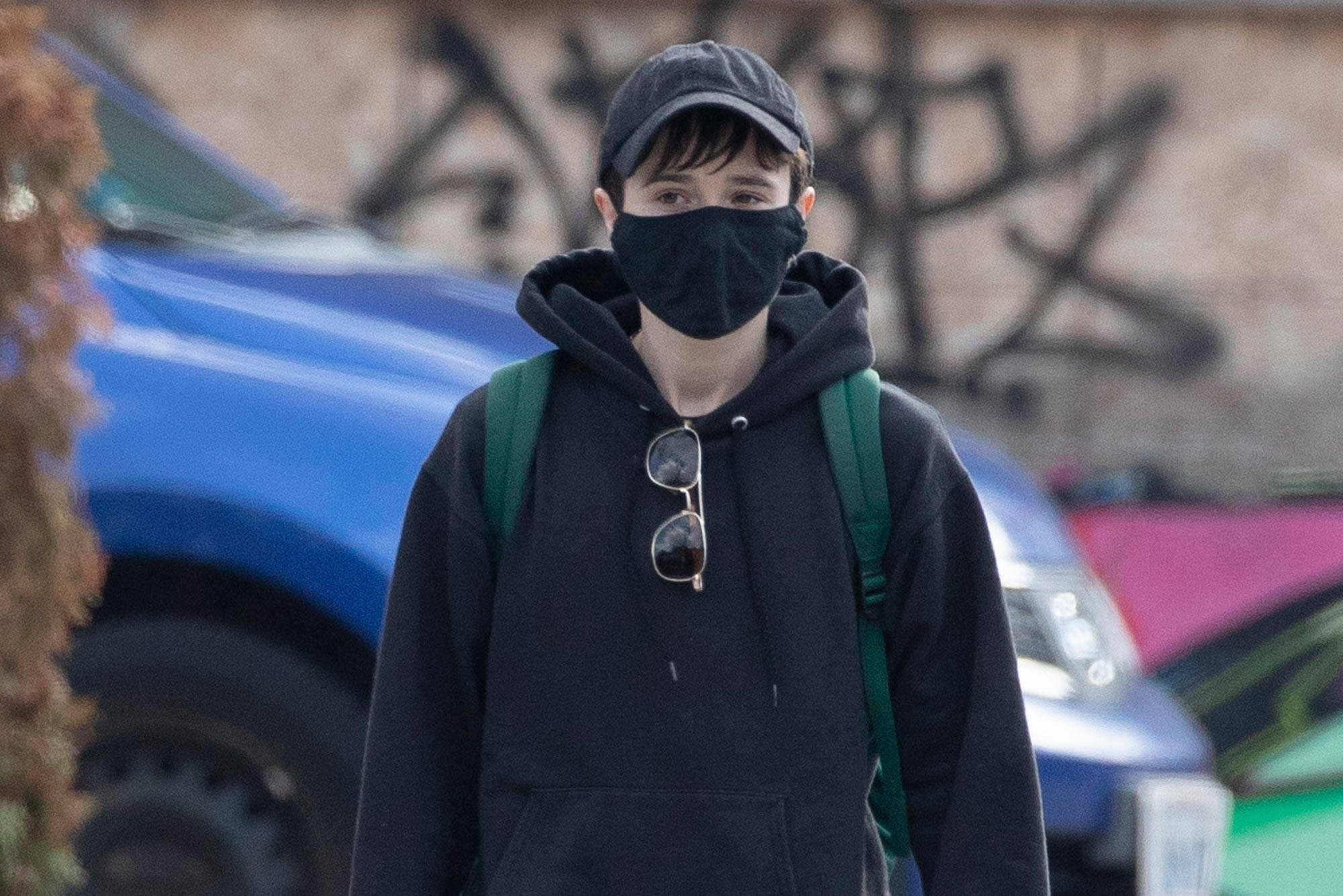 Elliot 桌布 壁紙 — 一個穿著黑色連帽衫和口罩的年輕人走過塗鴉牆，背景是色彩繽紛的汽車。