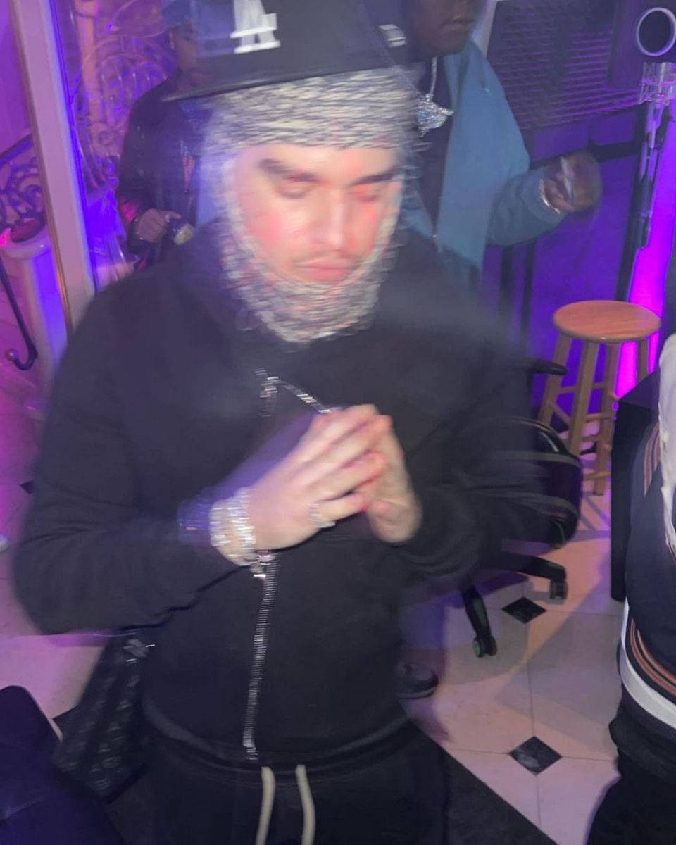  壁紙 — 一個穿著黑色連帽衫和鎖子甲頭罩的人站在燈光昏暗、有紫色燈光和木凳的俱樂部裡。
