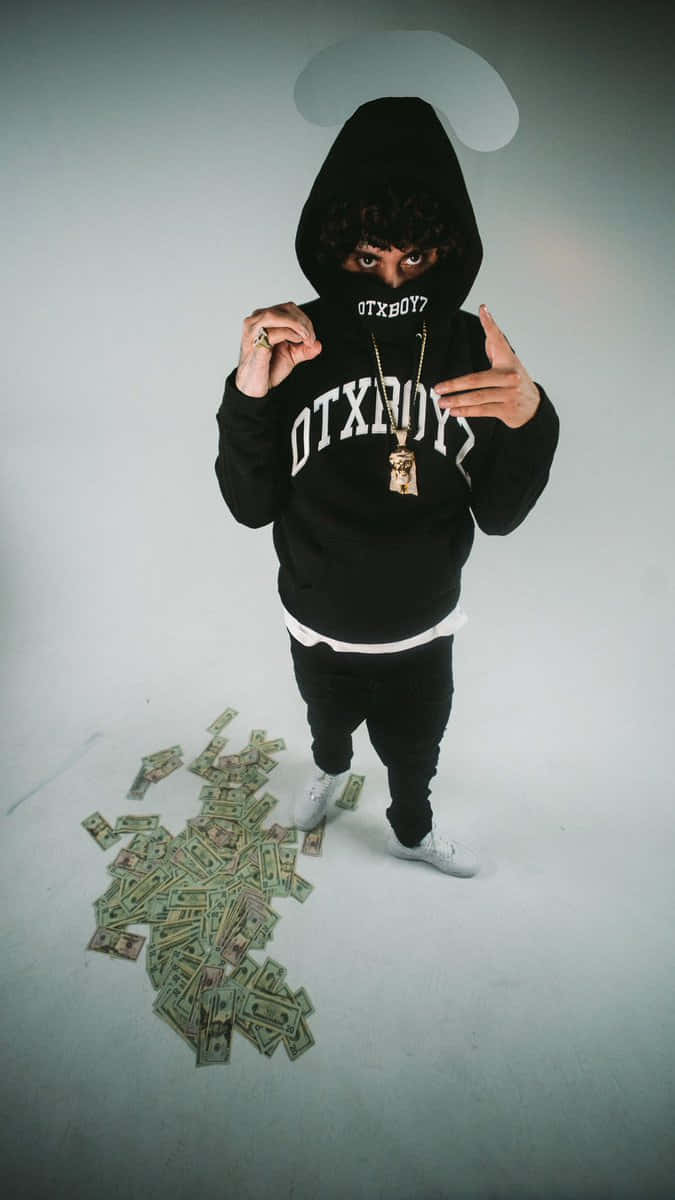 Shoreline Mafia 桌布 壁紙 — 一個穿著黑色連帽衫的人，地上散落著金錢，頭頂有光環擺姿勢。