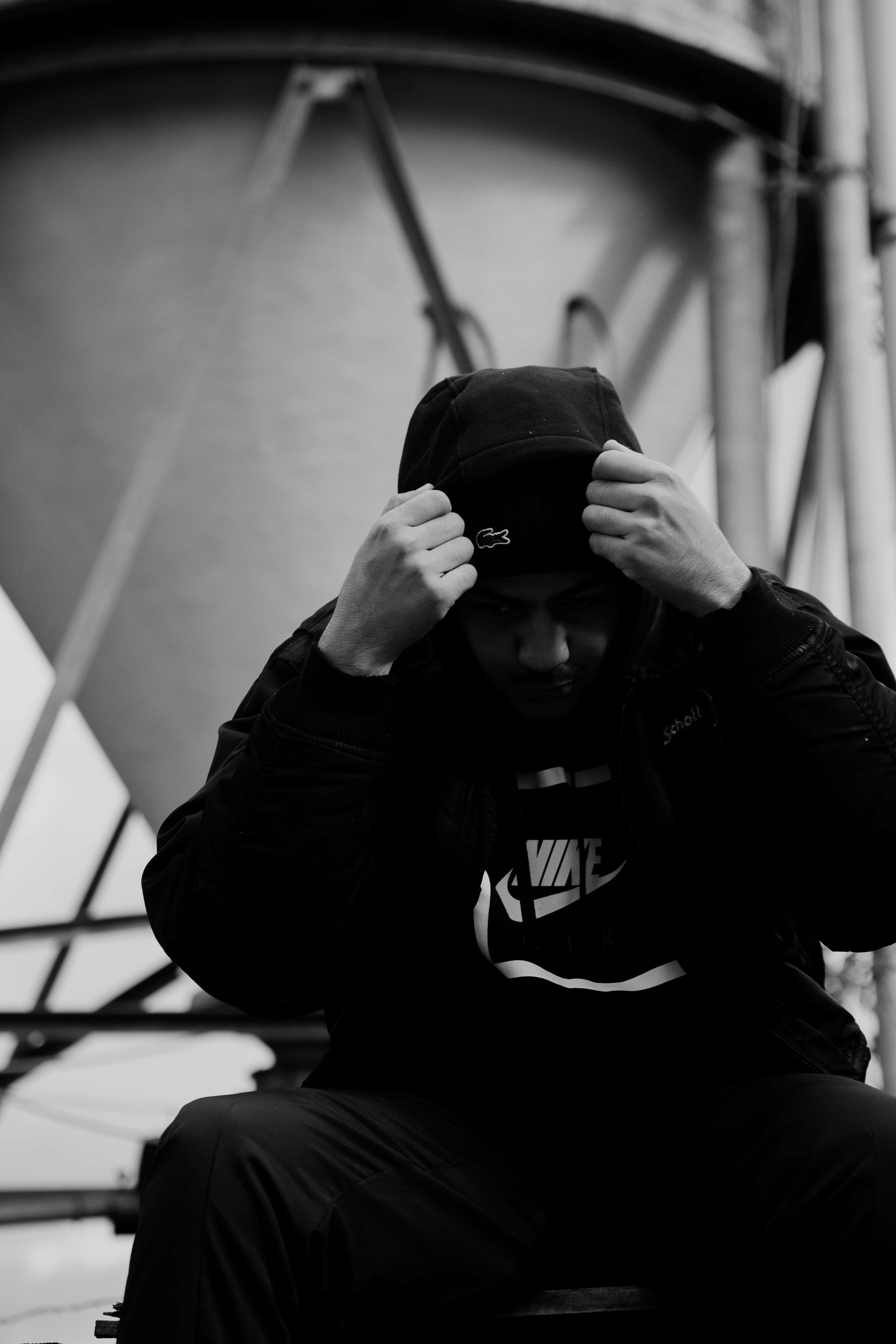 Bad Vibes 桌布 壁紙 — 一個穿著黑色連帽衫的人，坐在簡樸的工業環境中，將帽子拉過頭頂。