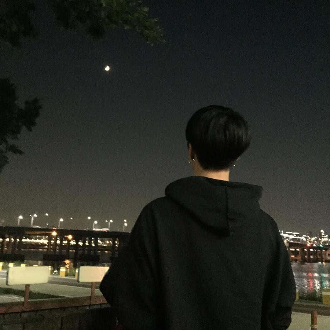 暗黑風格 桌布 壁紙 — 一個穿著黑色連帽衫的人夜晚站在城市上空凝視著新月，城市燈火輝煌。
