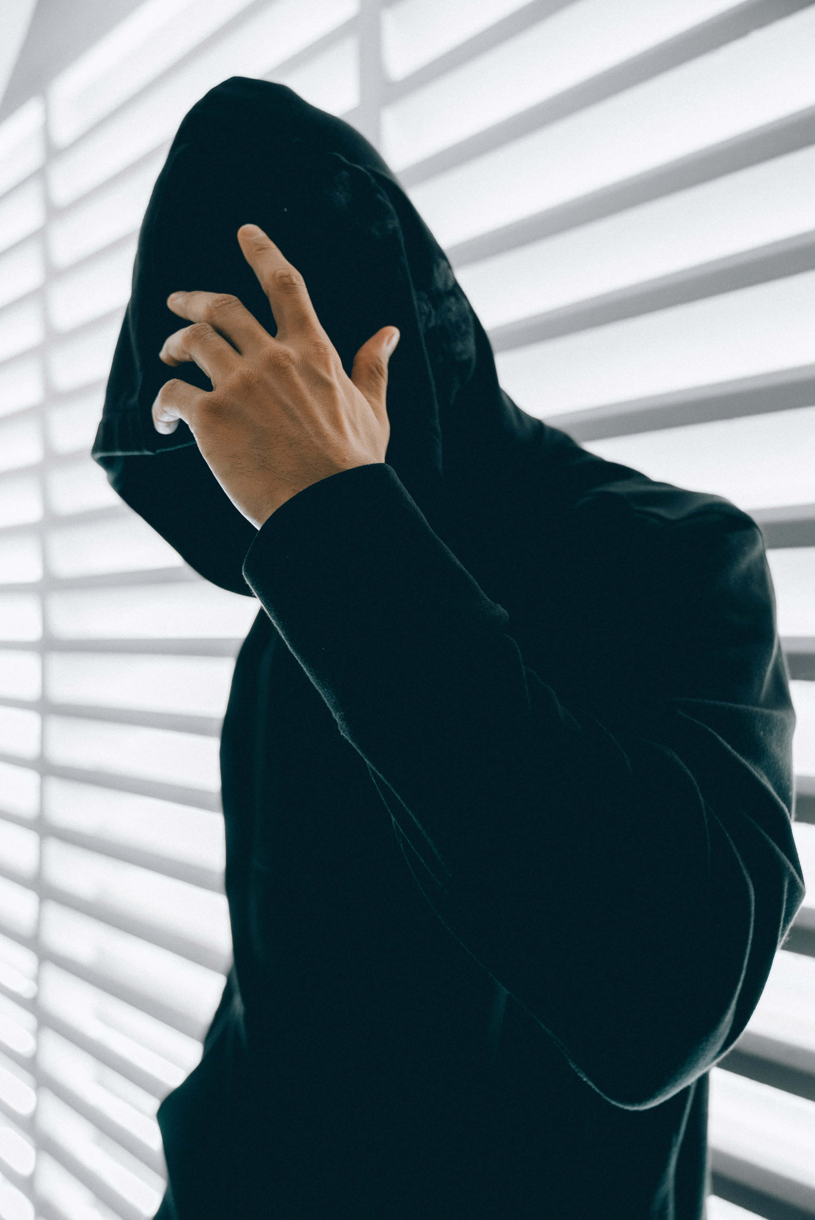 Man 桌布 壁紙 — 一個穿著黑色連帽衫的人將帽子拉過臉部，對著明亮的水平百葉窗。