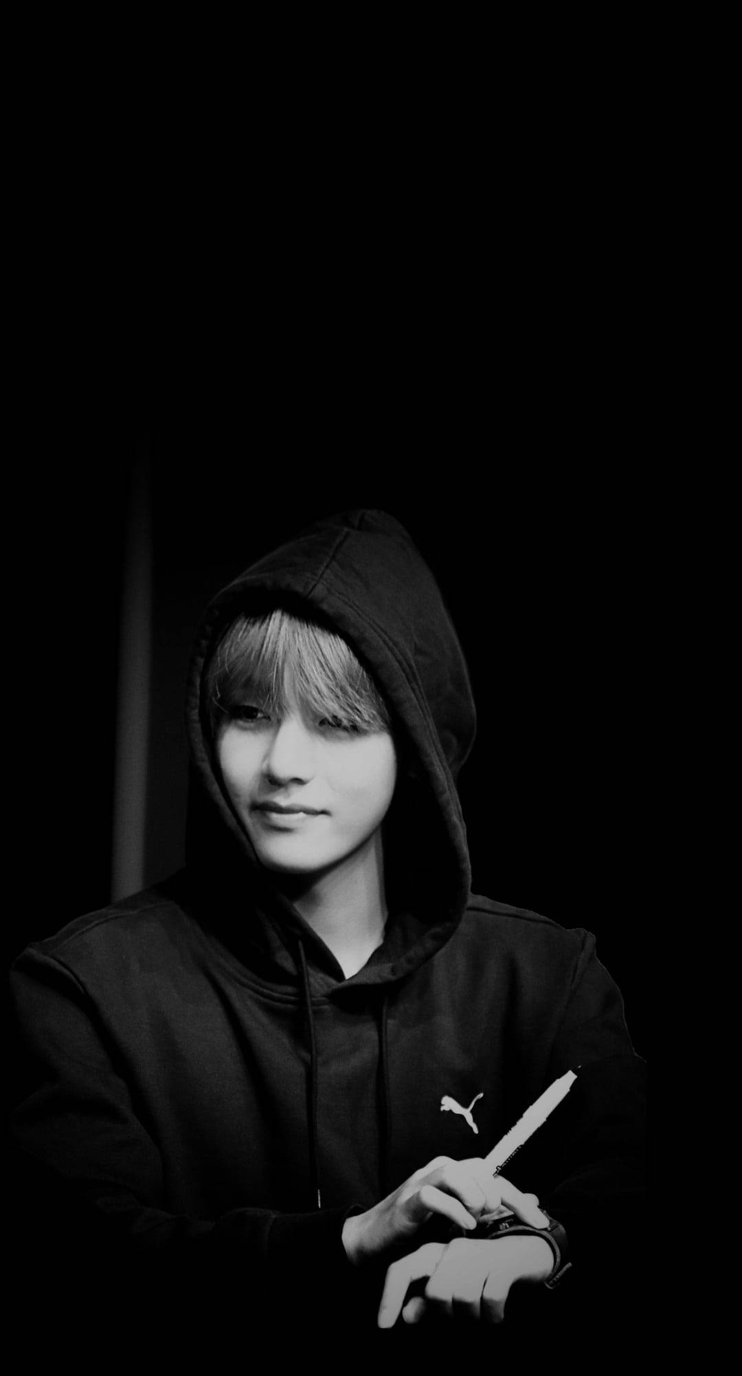 BTS 鎖定螢幕 桌布 壁紙 — 一個穿著黑色連帽衫的年輕人，在 stark 黑色背景下拿著一把刀，營造出陰鬱的黑白肖像。