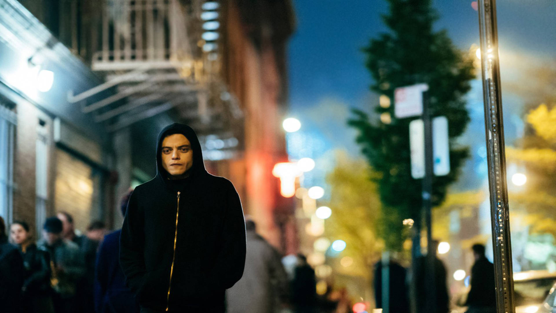 Mr Robot 桌布 壁紙 — 一個穿著黑色連帽衫的年輕男子夜晚獨自站在繁忙的城市街道上，被溫暖的路燈和發光的招牌照亮。