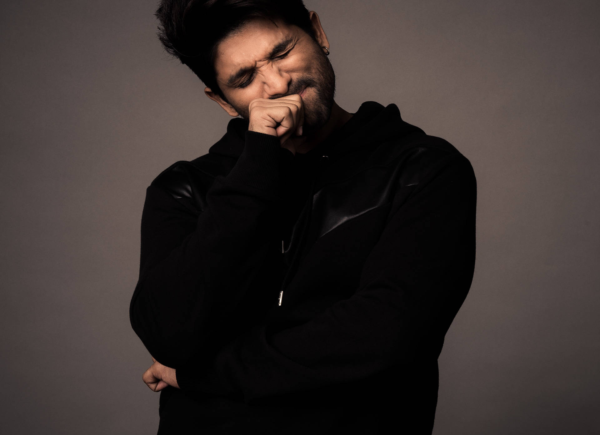 Allu Arjun 桌布 壁紙 — 一個穿著黑色連帽衫的男人在柔和的灰色背景前用手摀住嘴。
