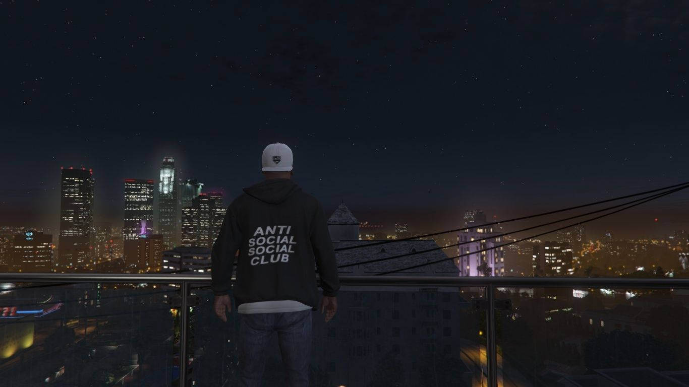 club 桌布 壁紙 — 一個穿連帽衫的人夜晚站在屋頂上，俯瞰著星空下燈火輝煌的城市景觀。