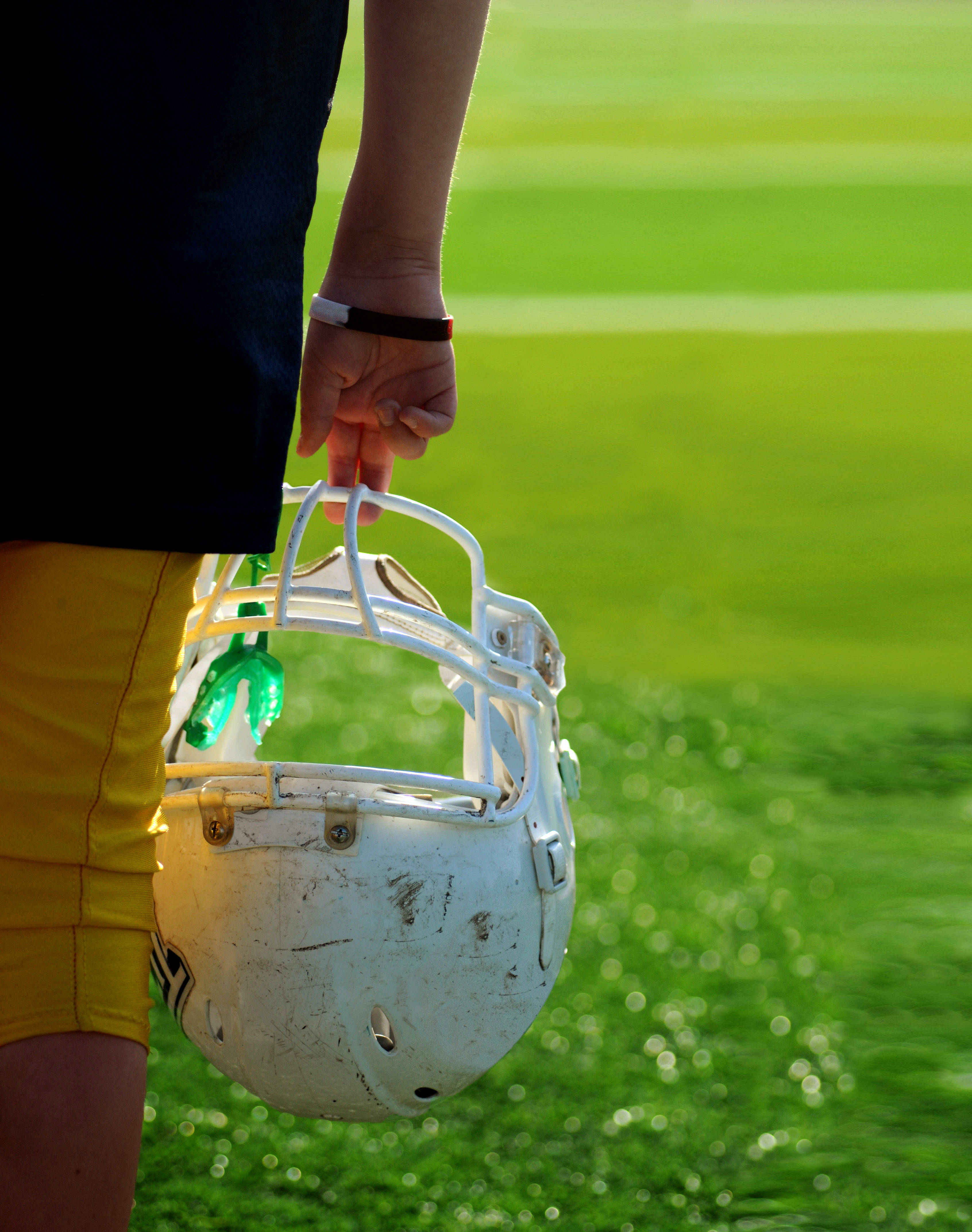 NFL 桌布 壁紙 — 一個穿黃色短褲的人拿著一個白色美式足球頭盔，裡面塞著一個綠色水壺，背景是陽光照耀的綠色球場。