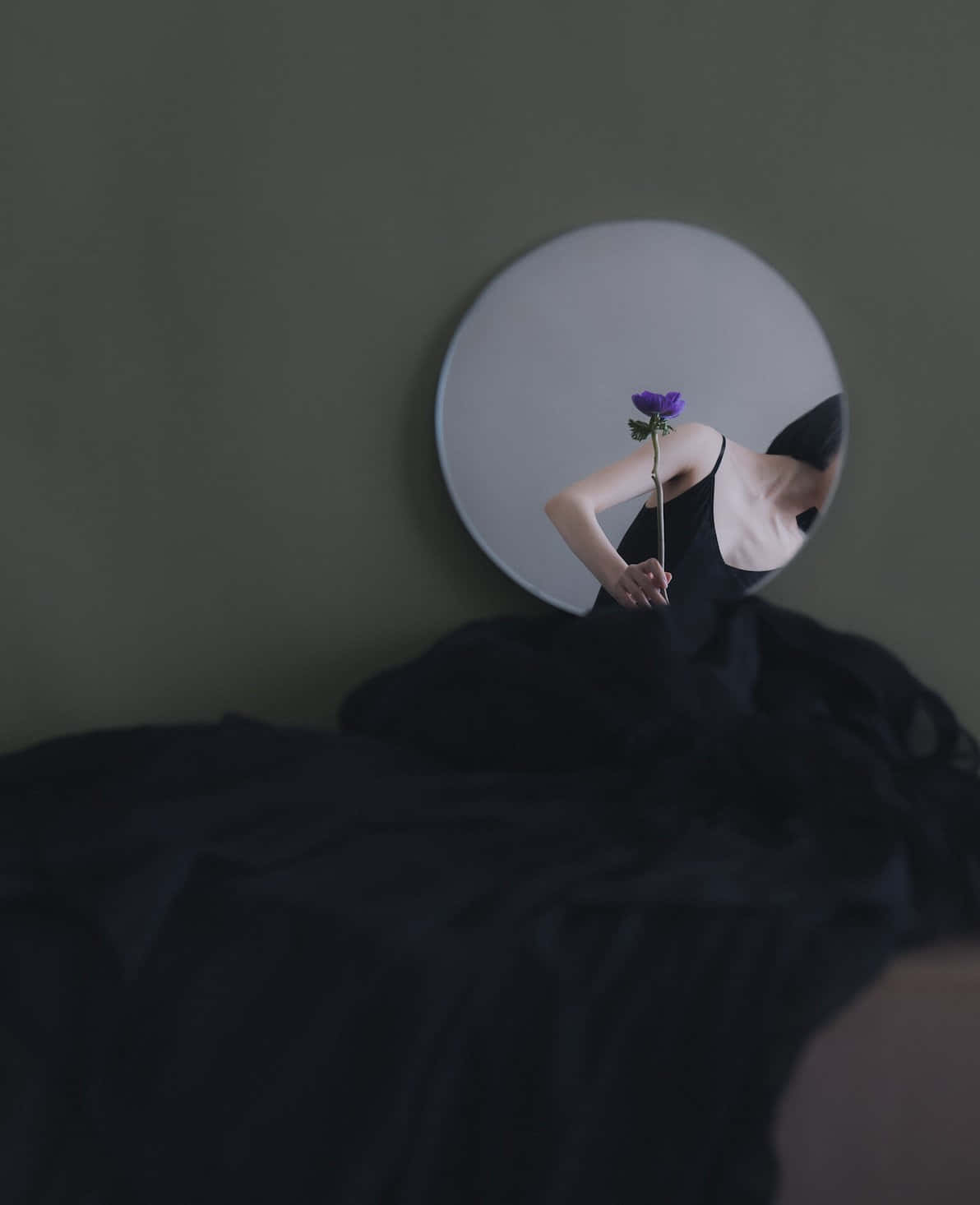 reflection 桌布 壁紙 — 一個穿黑色衣服的人拿著一朵紫色花，映照在圓鏡中，背景是柔和的綠色牆壁。