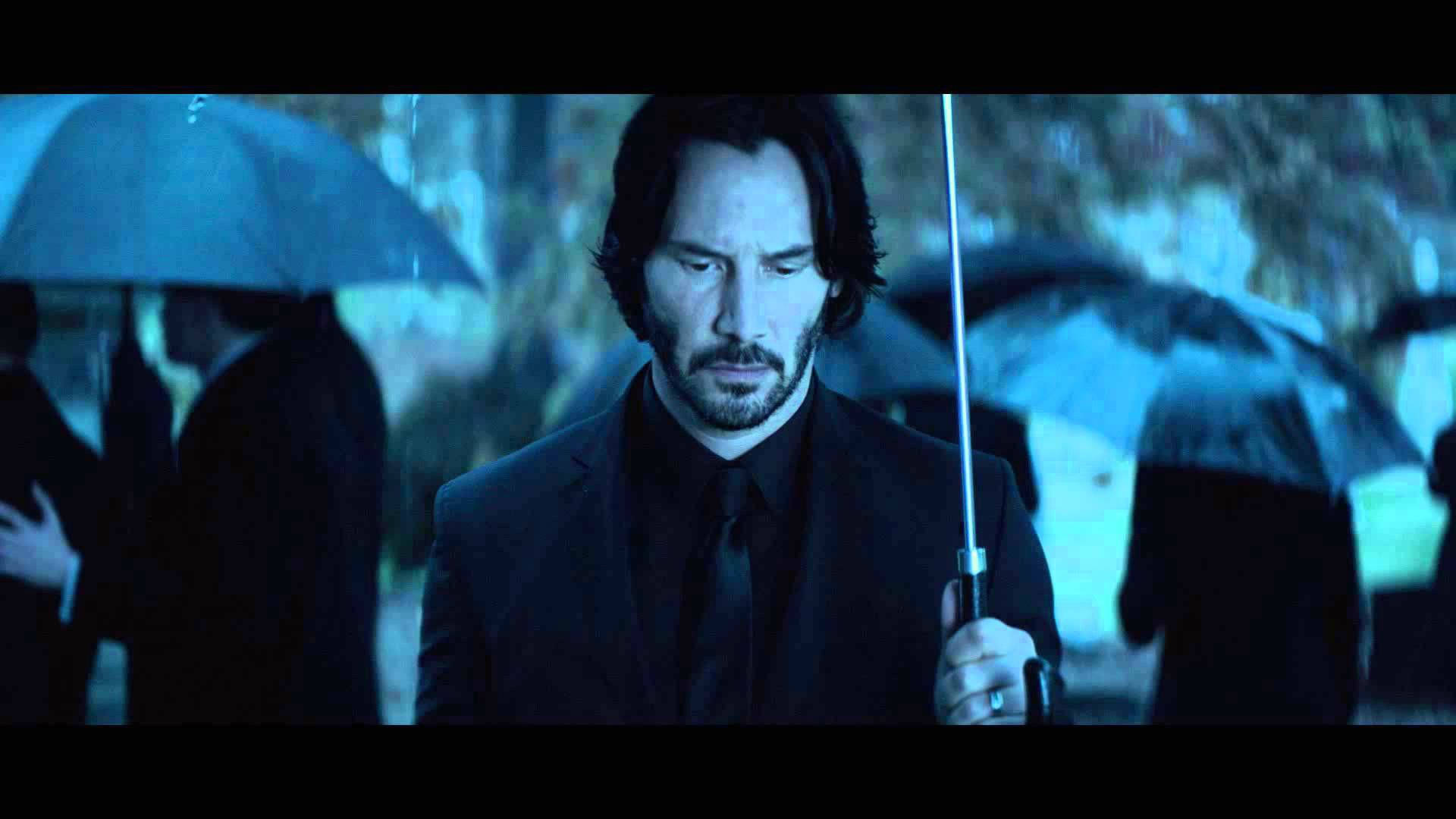 John Wick 桌布 壁紙 — 一個穿黑色西裝的男人在雨中的街燈下撐著傘，背景有模糊的人影。