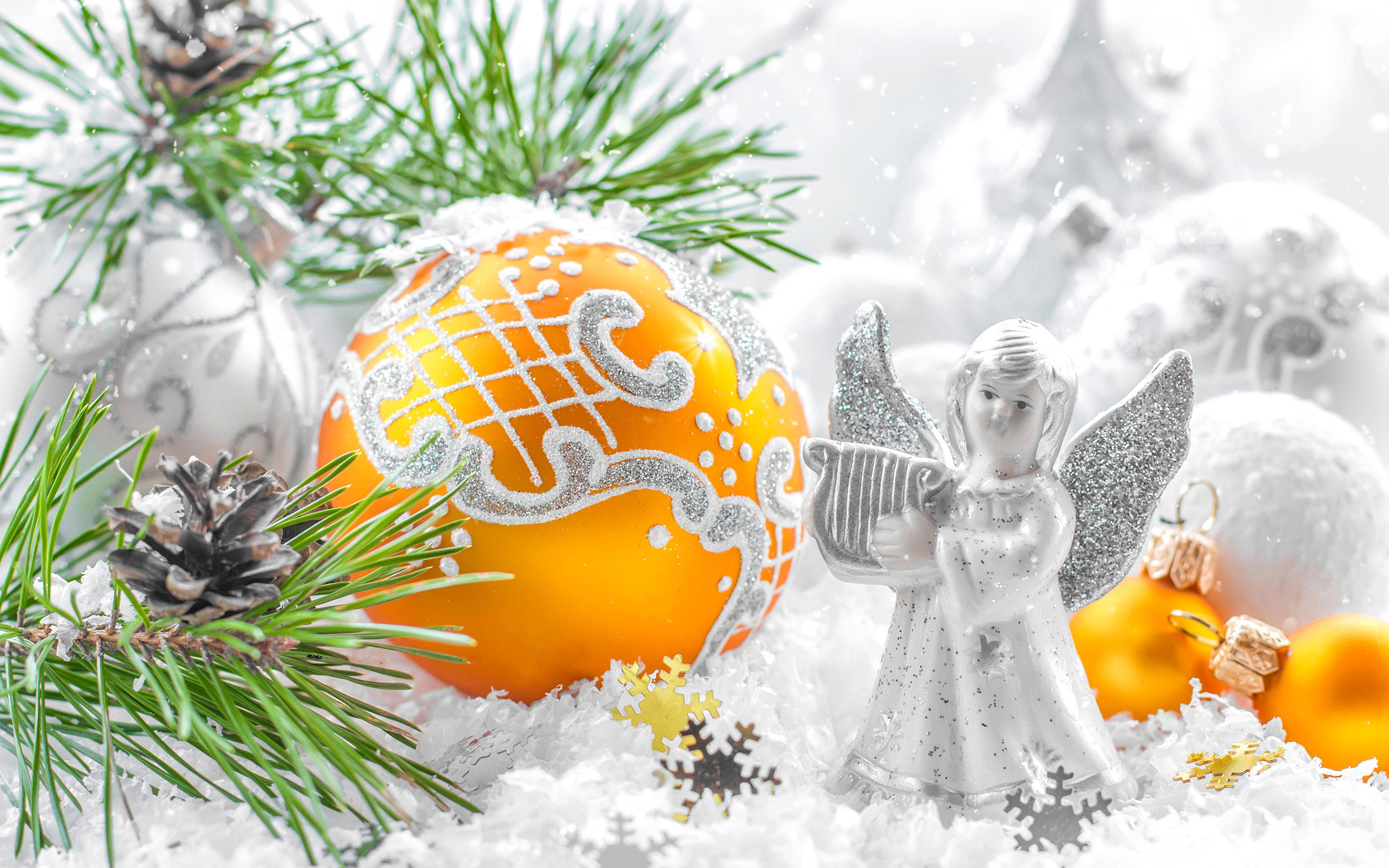 angels 桌布 壁紙 — 一個節日冬季場景，閃閃發光的銀色天使雕像旁邊有一個橙色裝飾品和灑滿雪的松樹枝。