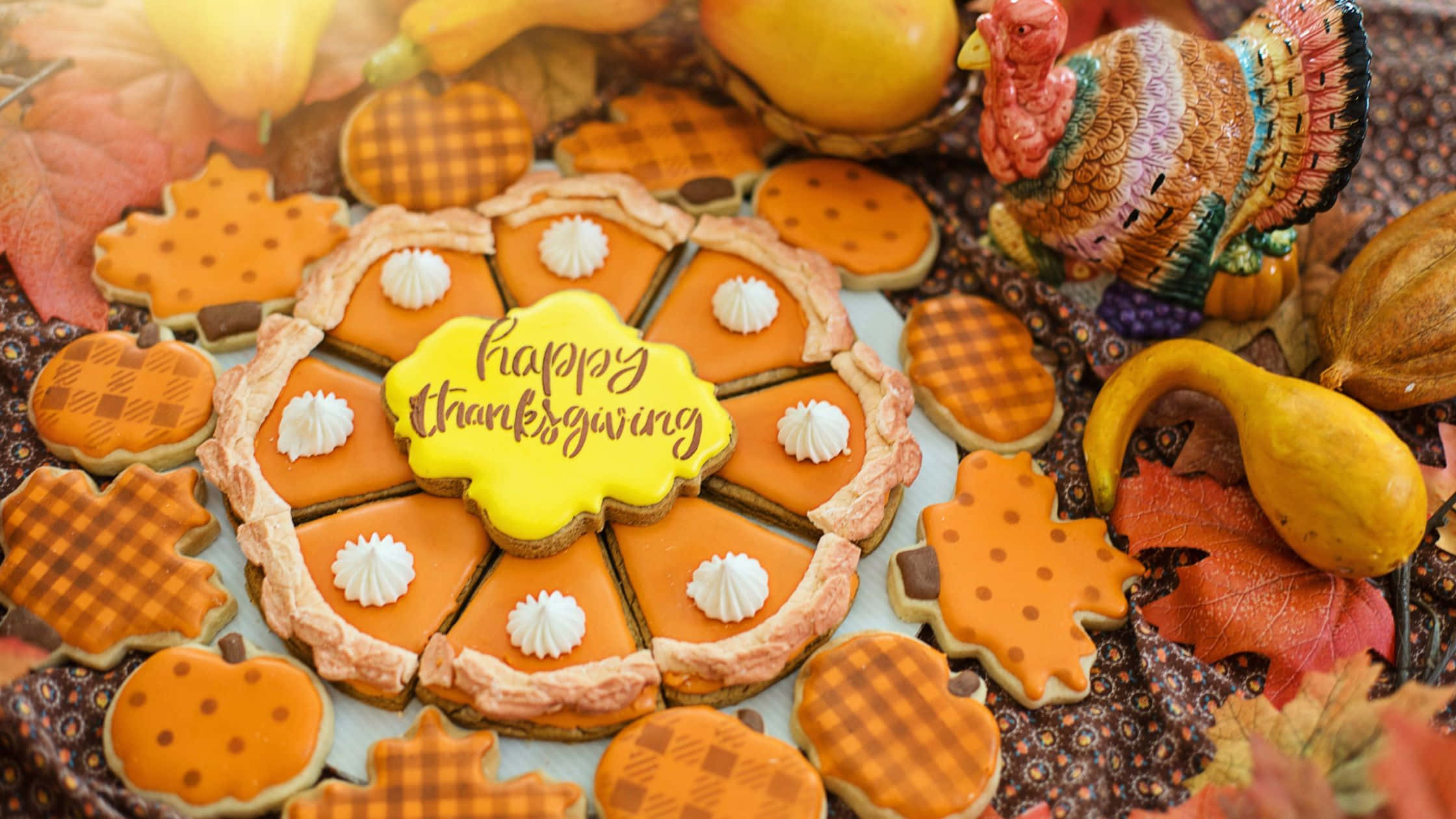 Thanksgiving Desktop 桌布 壁紙 — 一個節日感恩節拼盤，包含南瓜形狀的餅乾配鮮奶油，以及中央的「Happy Thanksgiving」餅乾，周圍環繞著秋葉和陶瓷火雞。
