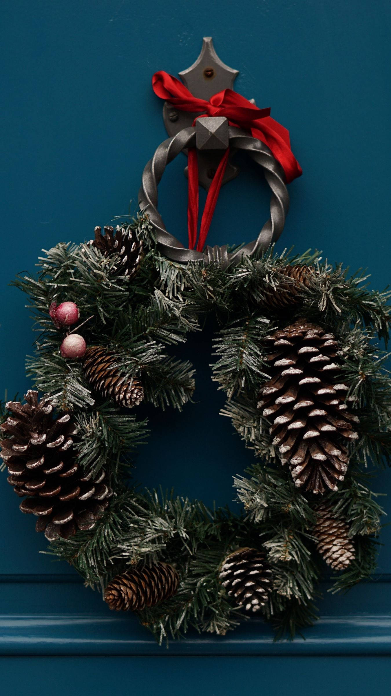 Wreath 桌布 壁紙 — 一個節日松果花環，帶有紅色絲帶，掛在深藍綠色門環上，襯著一扇濃郁的藍色門。