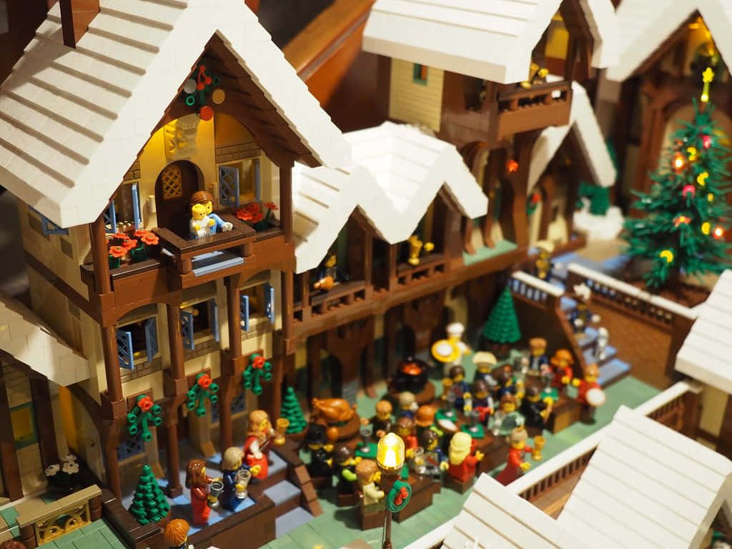 Christmas Village 桌布 壁紙 — 一個節日氣氛濃厚的LEGO冬季村莊，有積雪覆蓋的屋頂、閃爍的燈光，以及圍繞著裝飾樹慶祝的小人偶。