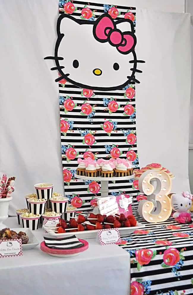 Hello Kitty Party 桌布 壁紙 — 一個節日氣氛的Hello Kitty生日派對佈置，配有條紋粉紅色花卉裝飾、杯子蛋糕和一個發光的三字。