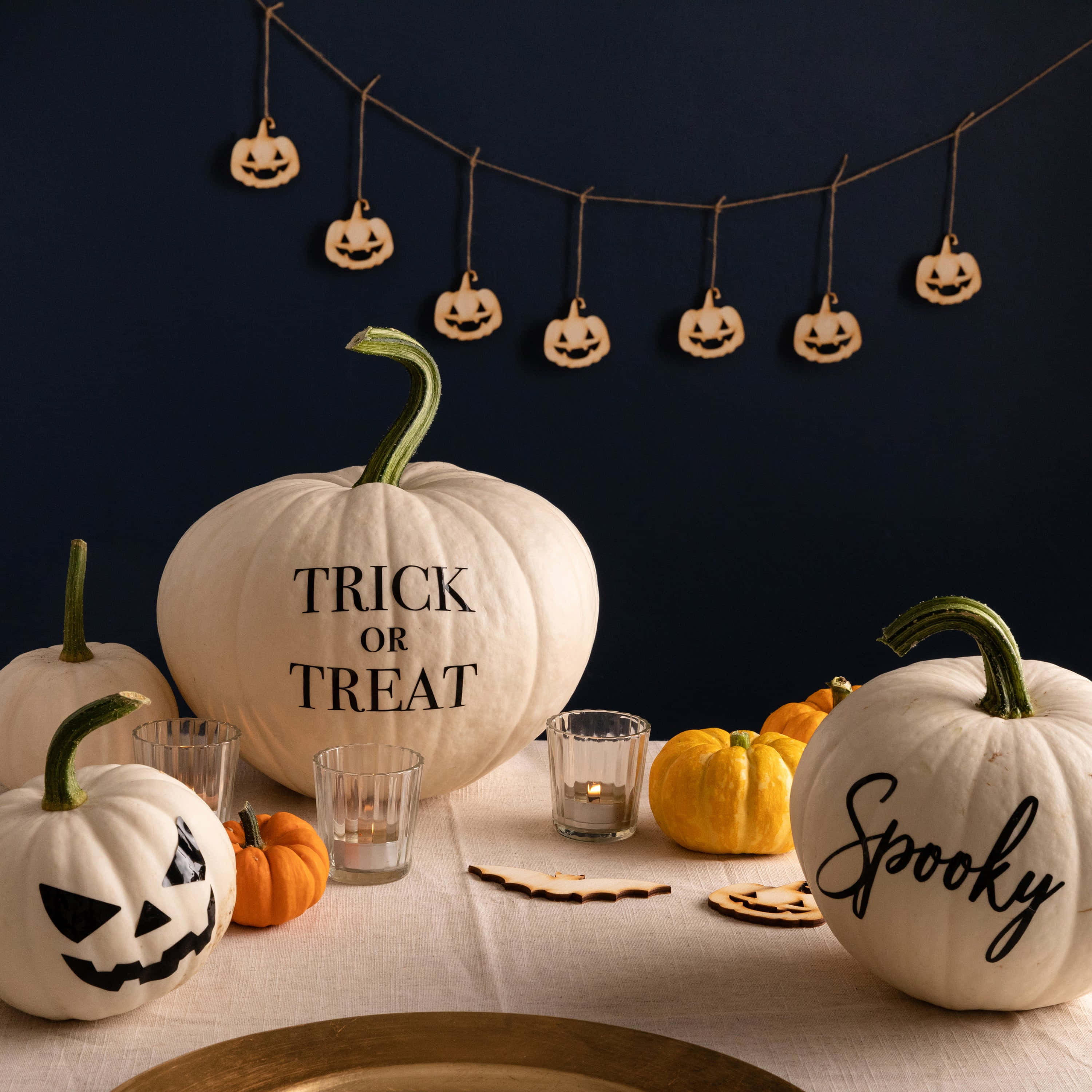 萬聖節動圖 桌布 壁紙 — 一個節日氣氛的萬聖節餐桌，擺放著標有 trick or treat 的白色南瓜，以及掛在深藍色牆壁上的恐怖傑克南瓜燈裝飾。