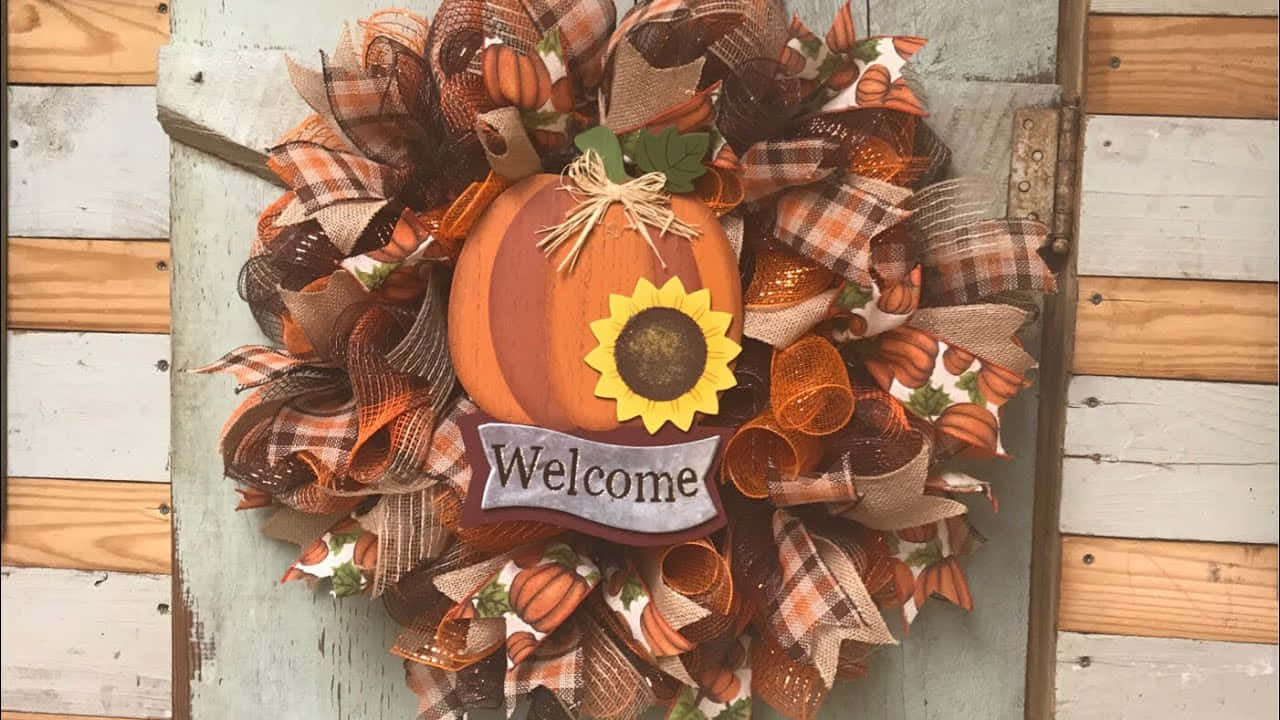 Fall Wreath 桌布 壁紙 — 一個節日秋季花環，上面有南瓜、向日葵和格子絲帶，掛在風化的木門上。