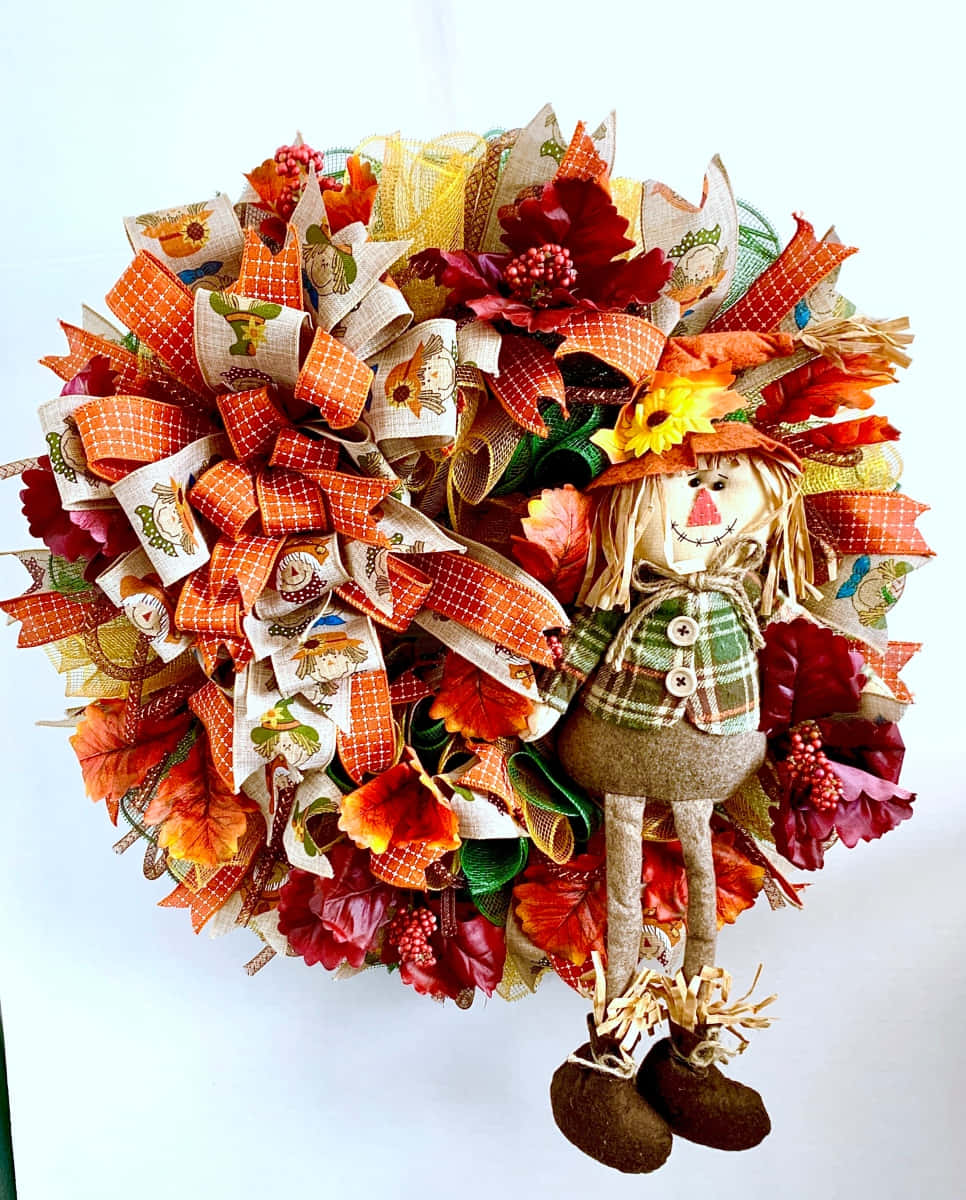 Fall Scarecrow 桌布 壁紙 — 一個節日秋季花環，飾有橙色格子絲帶、秋葉和一個歡樂的稻草人形象。