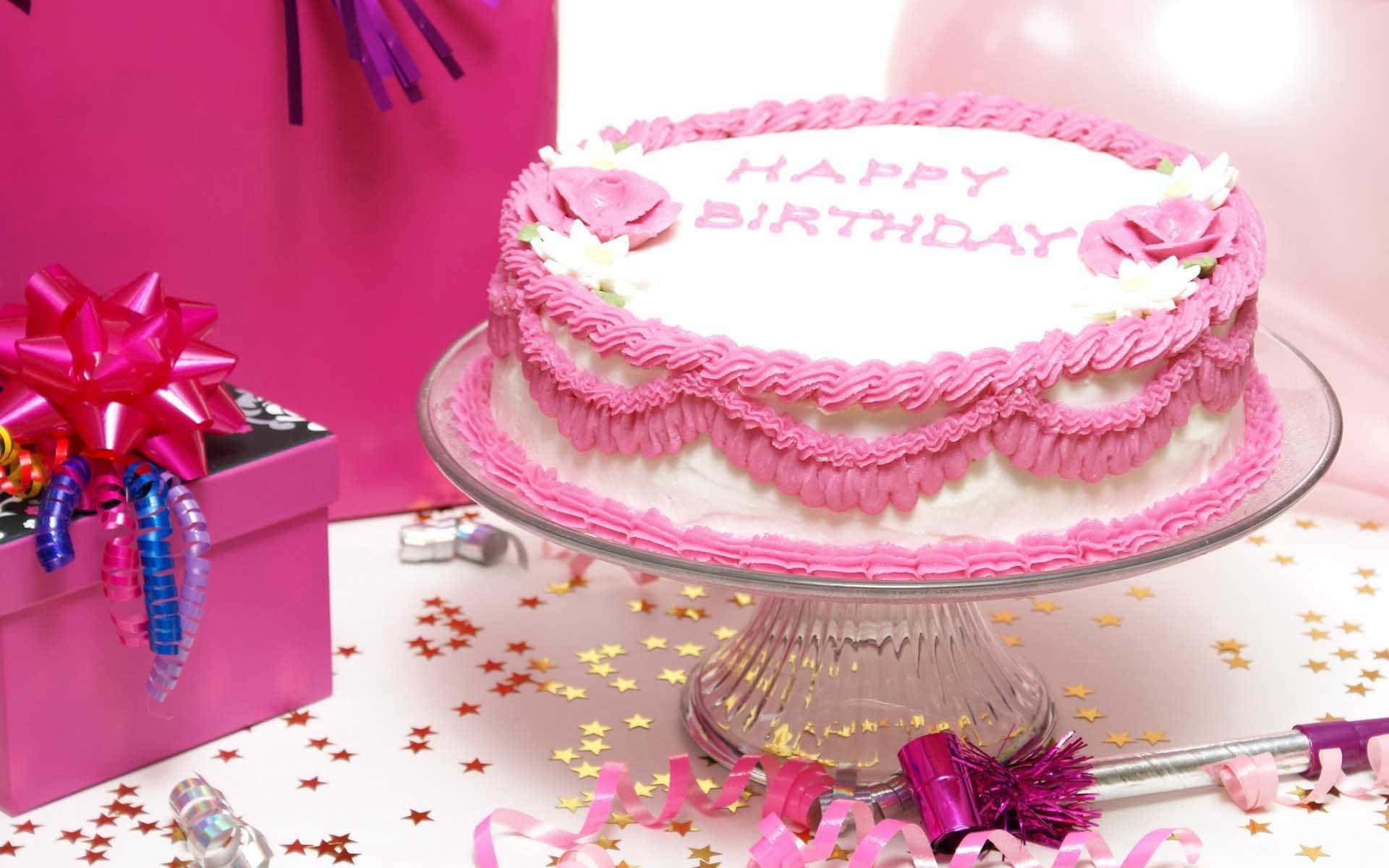 Pink Birthday 桌布 壁紙 — 一個節日粉紅色生日蛋糕，帶有裱花糖霜和花朵，放在玻璃架上，旁邊有一個禮物盒和五彩紙屑。