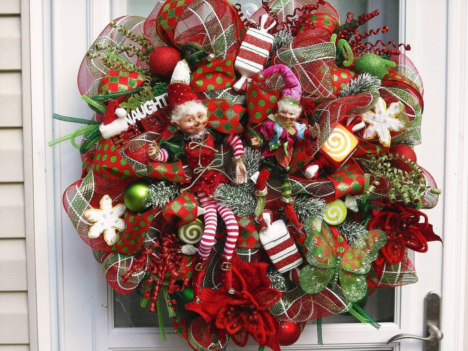 Wreath 桌布 壁紙 — 一個節日紅綠聖誕花環，飾有精靈、拐杖糖和裝飾品，掛在白色門上。