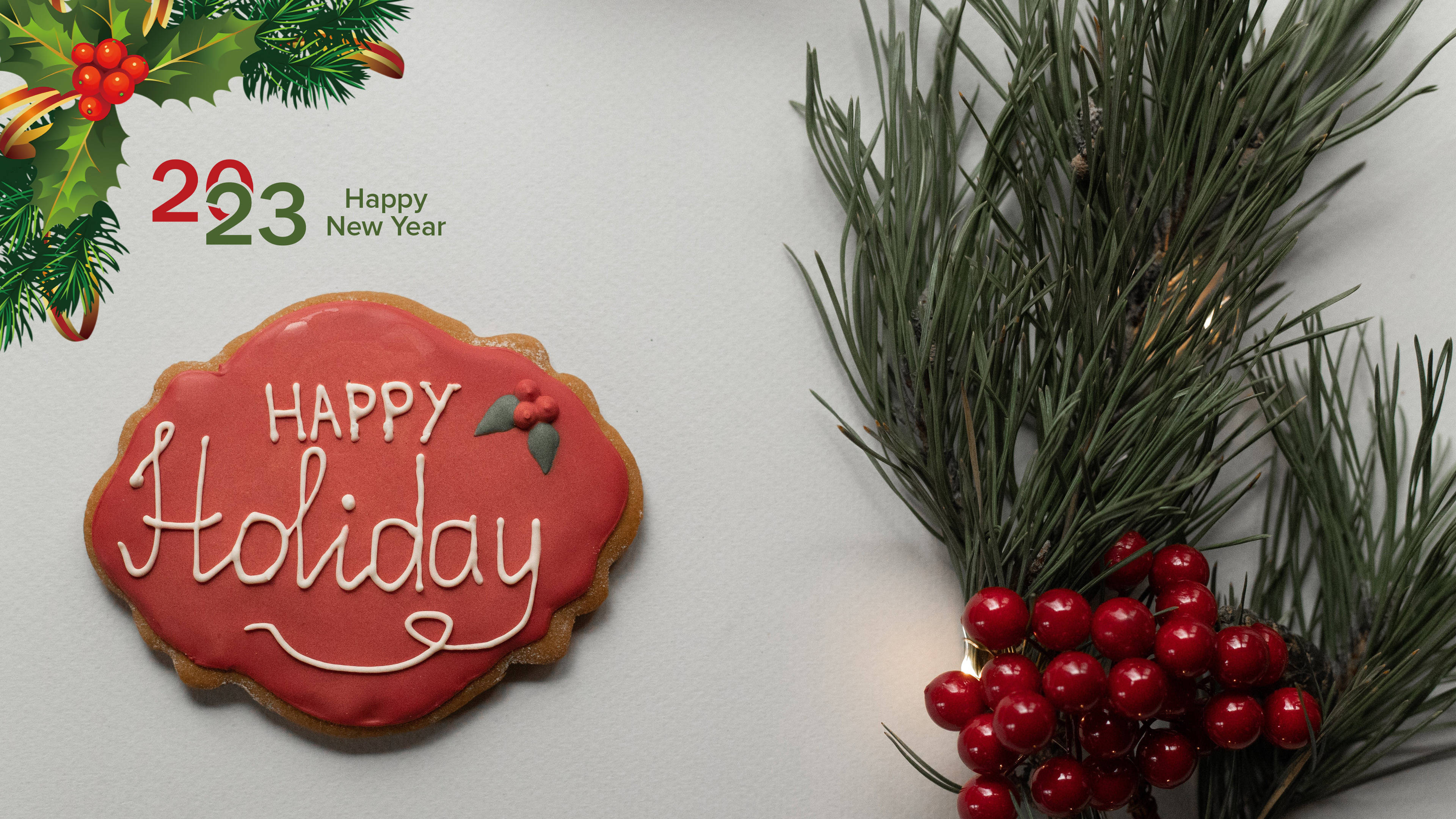 新年快樂 桌布 壁紙 — 一個節日紅色糖霜餅乾，上面有「Happy Holiday」字樣，旁邊有松枝和紅莓，放在白色表面上。