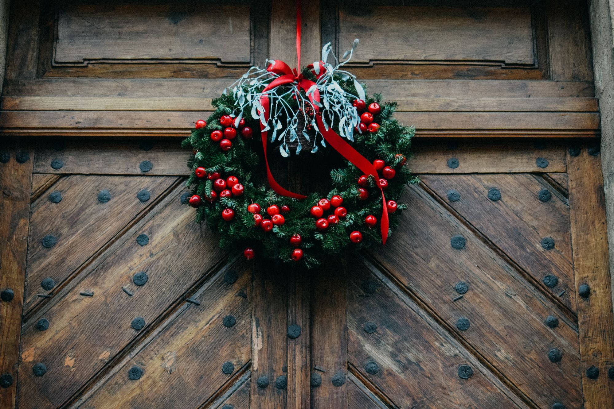 Wreath 桌布 壁紙 — 一個節日紅莓花環，配有紅色絲帶和銀色槲寄生，掛在帶有鐵釘的風化木門上。