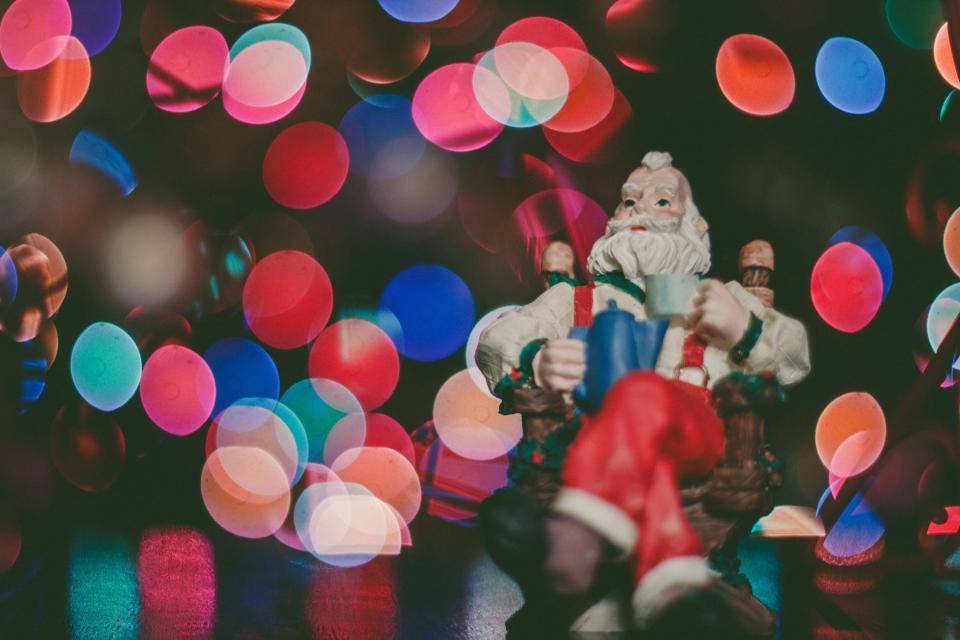 Santa Claus 桌布 壁紙 — 一個節日聖誕老人公仔在色彩繽紛的散景節日燈光背景下拿著一個馬克杯。