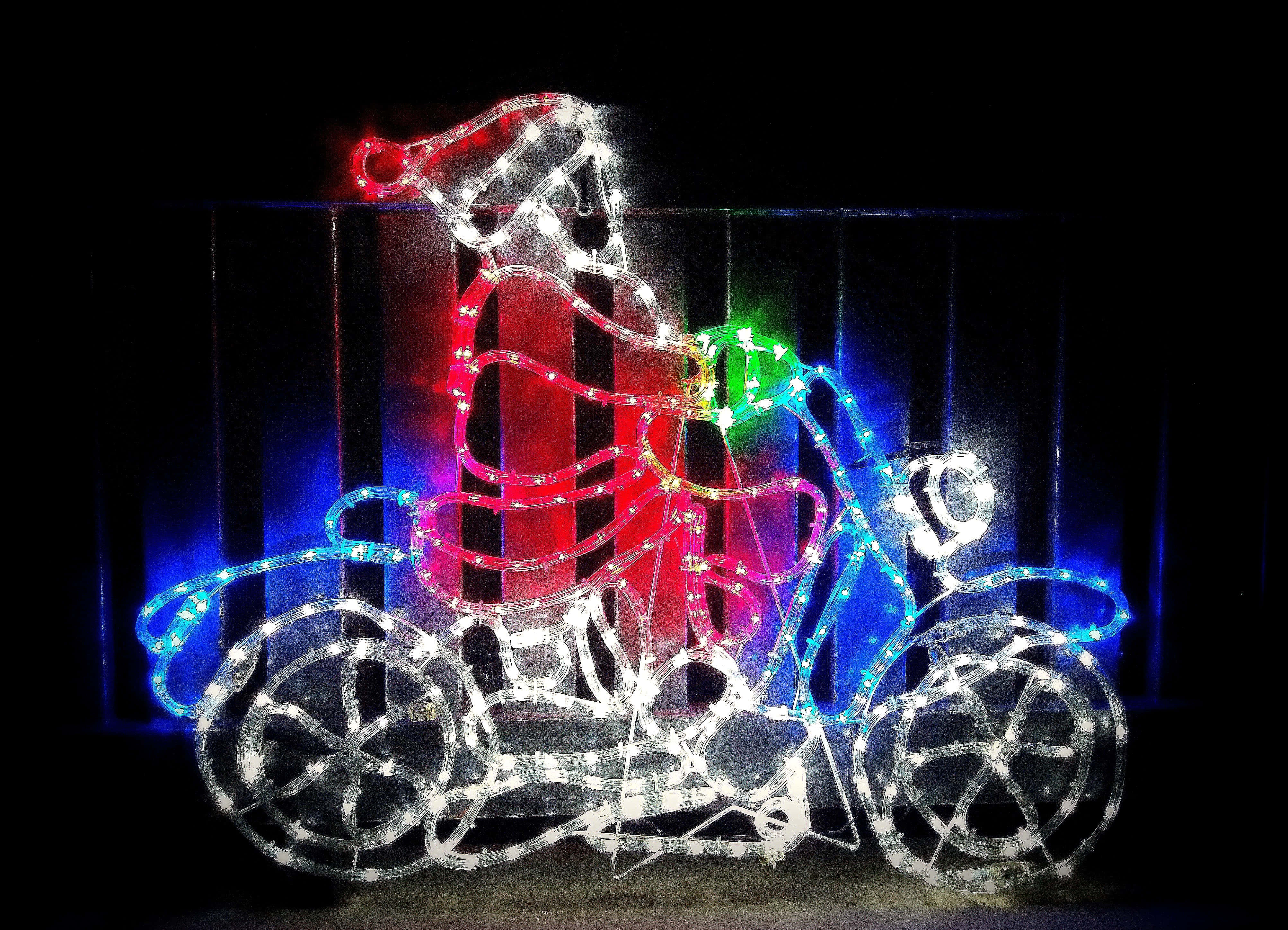 Christmas Light 桌布 壁紙 — 一個節日聖誕老人騎著三輪車，以發光的多色燈光勾勒出輪廓，背景為深色。