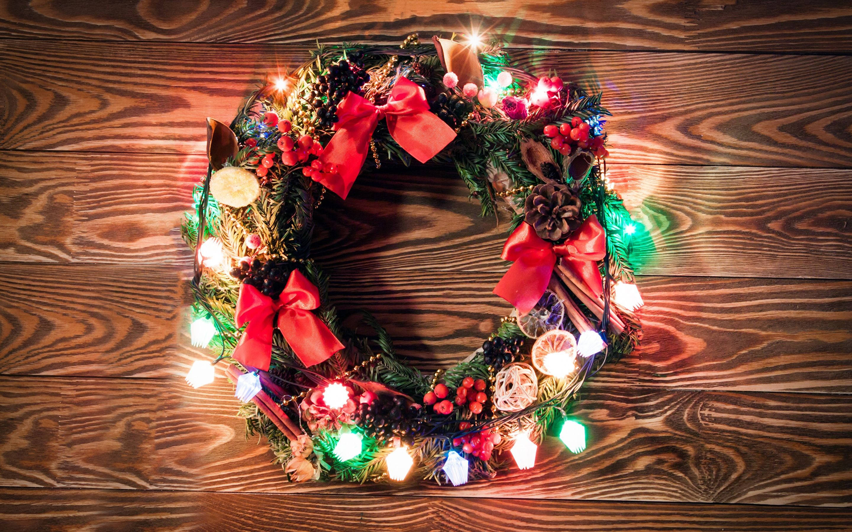 Wreath 桌布 壁紙 — 一個節日聖誕花環，飾有紅色蝴蝶結、松果和閃爍的燈光，放置在質樸的木質表面上。