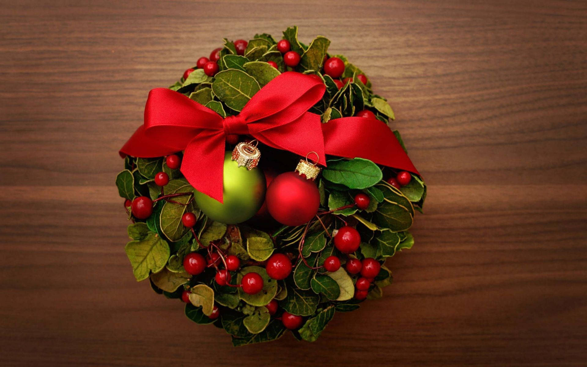 Wreath 桌布 壁紙 — 一個節日聖誕花環，飾有紅莓、綠葉和一個大紅色蝴蝶結，放置在溫暖的木質表面上。