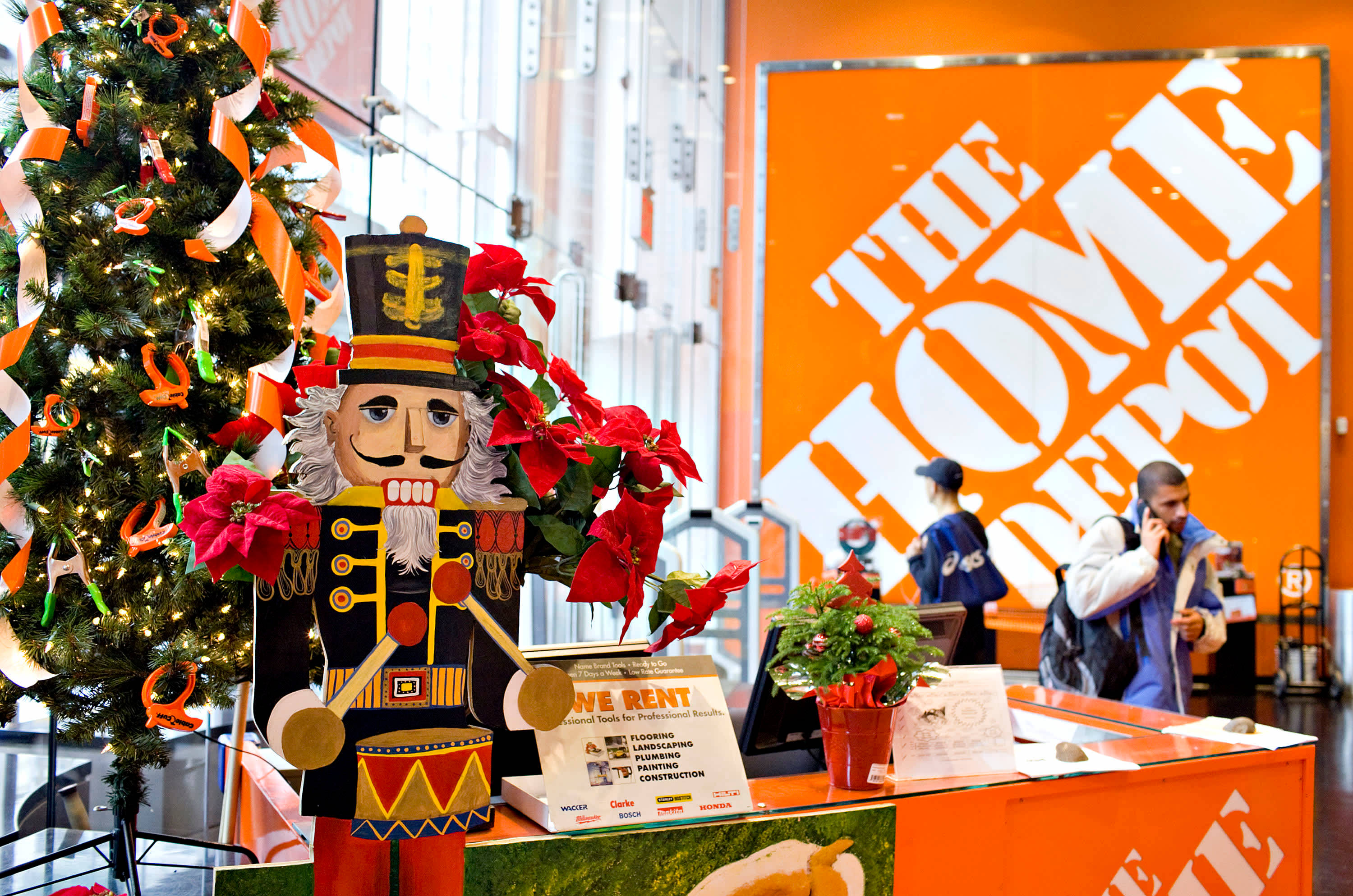 Home Depot 桌布 壁紙 — 一個節日胡桃夾子士兵站在裝飾好的聖誕樹旁，位於燈光明亮的Home Depot商店內。