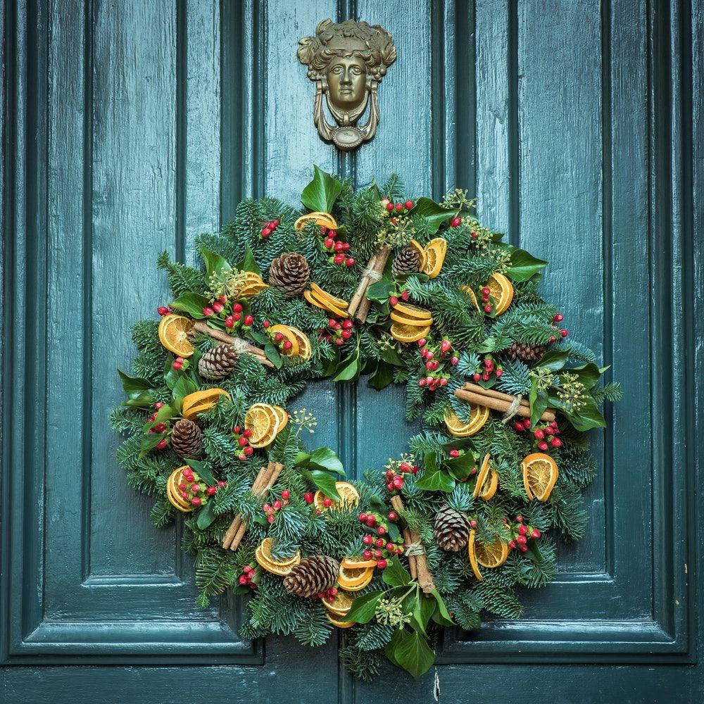 Wreath 桌布 壁紙 — 一個節日花環，裝飾著松果、乾橙片和紅莓，掛在一個風化的青綠色木門上，門上有黃銅門環。