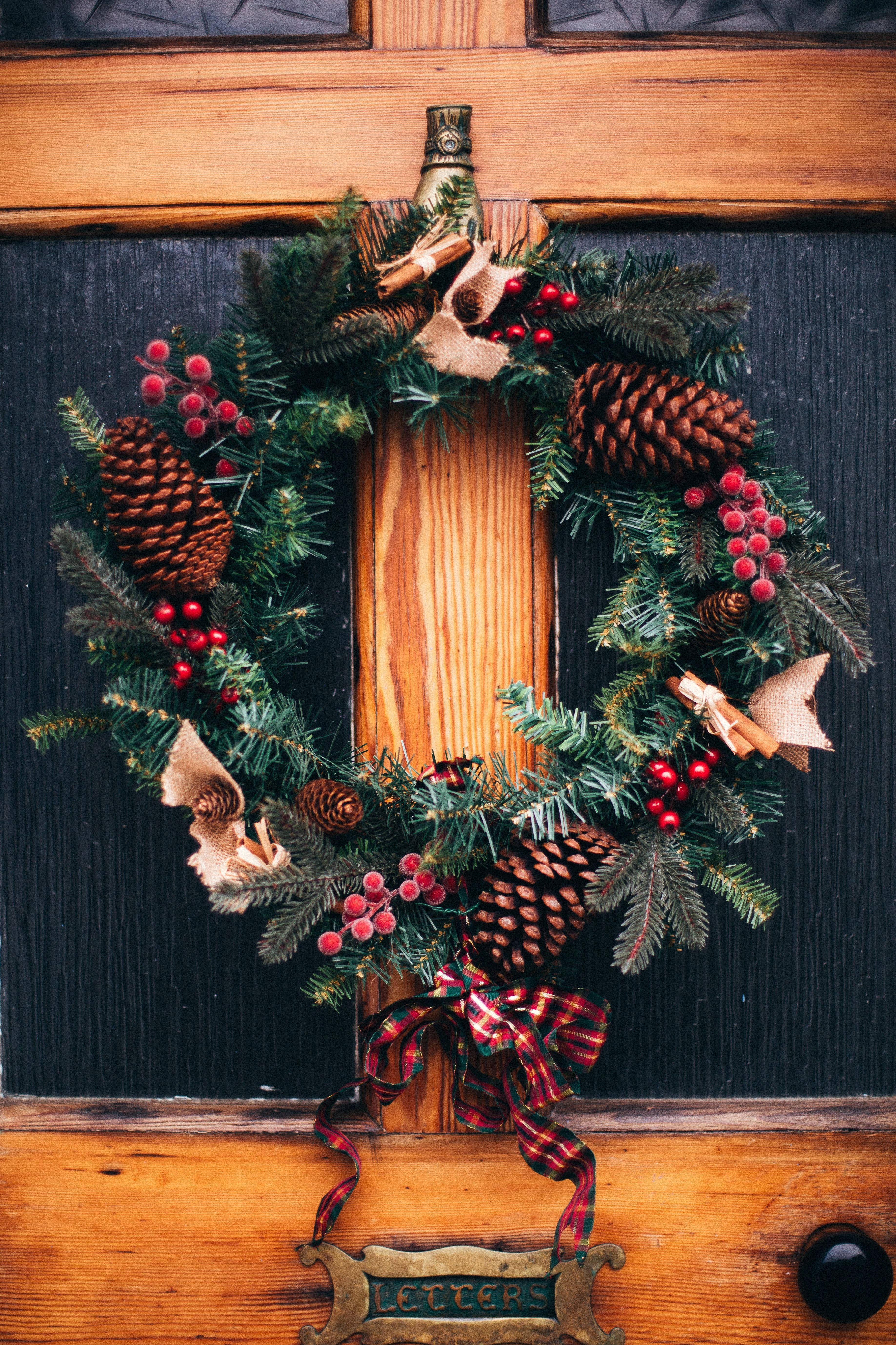 Wreath 桌布 壁紙 — 一個節日花環，裝飾著松果、紅莓、肉桂棒和格子絲帶，掛在質樸的木門上。
